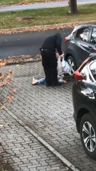 女孩躺在車子旁的地上，爸爸從座位拿完東西，下一秒直接彎腰揪着女兒的外套，直接把她拿起來。（ViralHog youtube截圖）