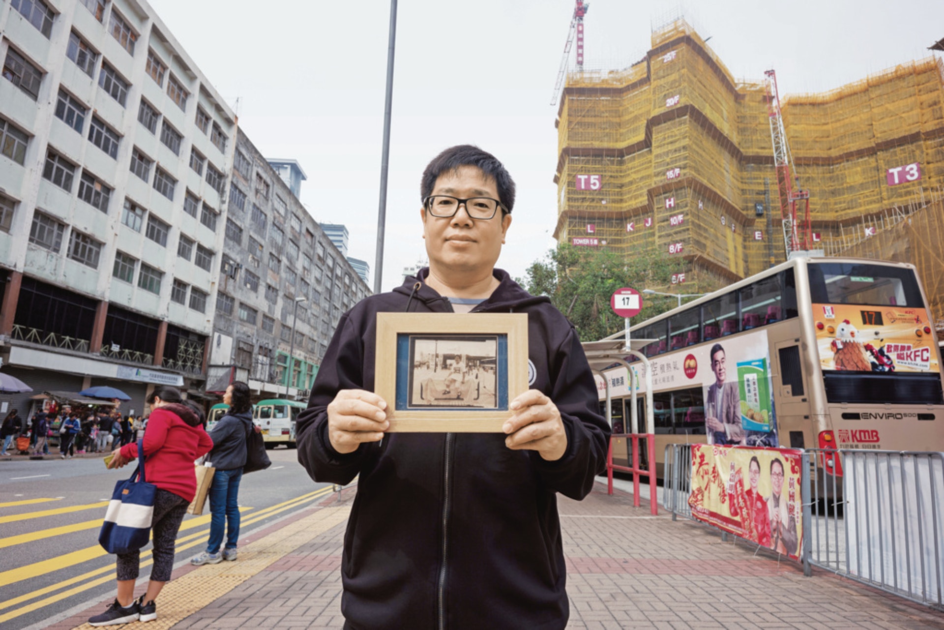 馮炳德拿着十二年前所拍的照片,站在即將重建的裕民坊和快落成的凱匯之間。(高仲明攝) 馮炳德拿着十二年前所拍的照片,站在即將重建的裕民坊和快落成的凱匯之間。(高仲明攝)