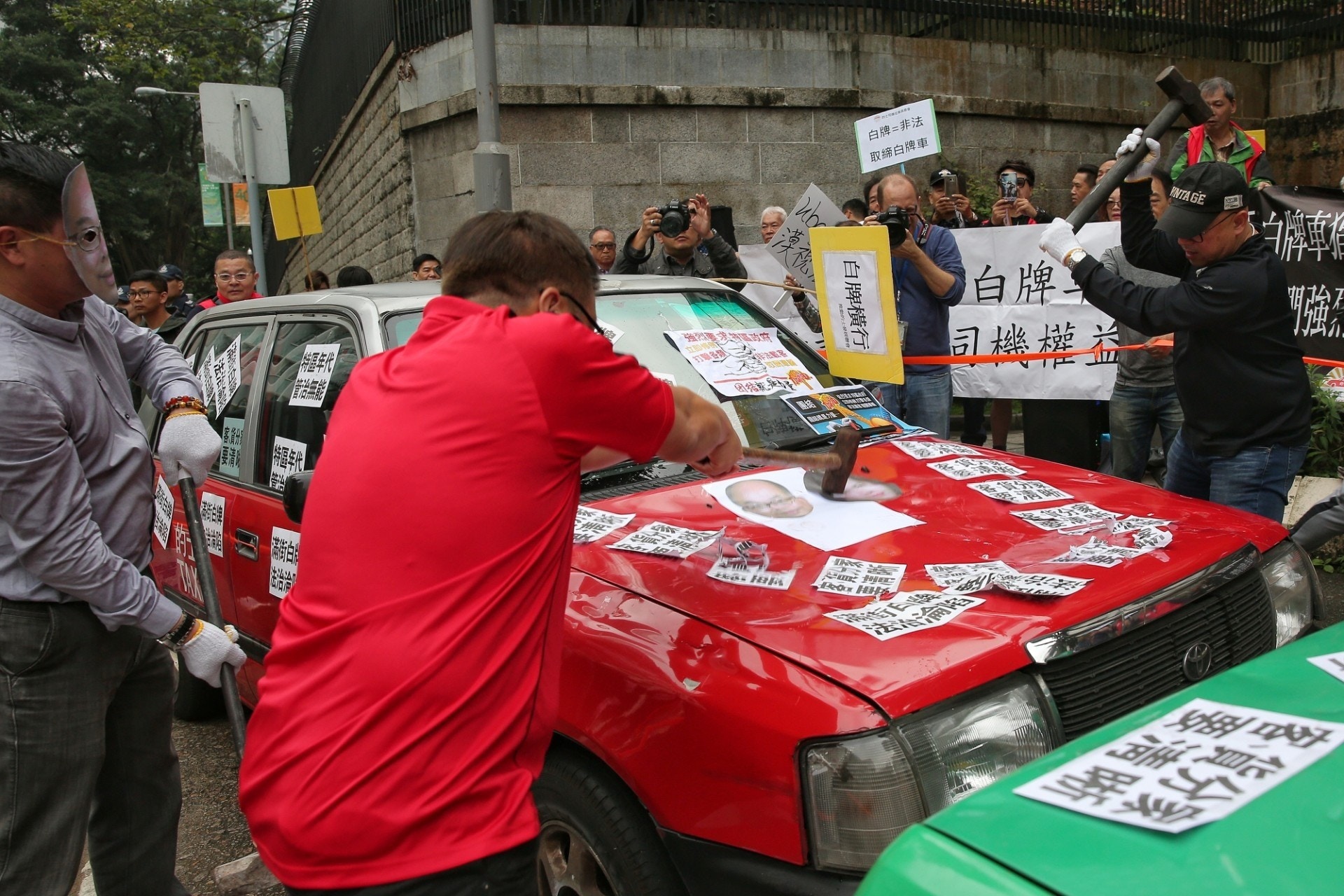 的士業界用鐵搥猛力敲打兩部的士車身及車頂至凹陷，意指遭Uber及白牌車「打爛飯碗」。（資料圖片）