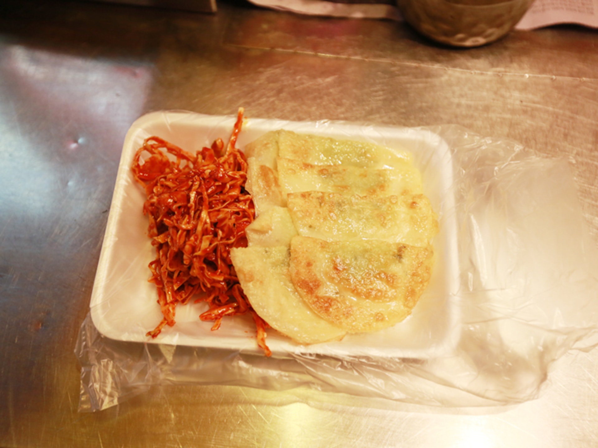 韭菜餡的偏平半圓的煎餃,在鐵板上煎成美味的金黃色,再捲著酸辣的白菜切絲和魷魚絲,酸甜微辣、爽口開胃的釜山特色小吃。(韓巢) (韓巢)