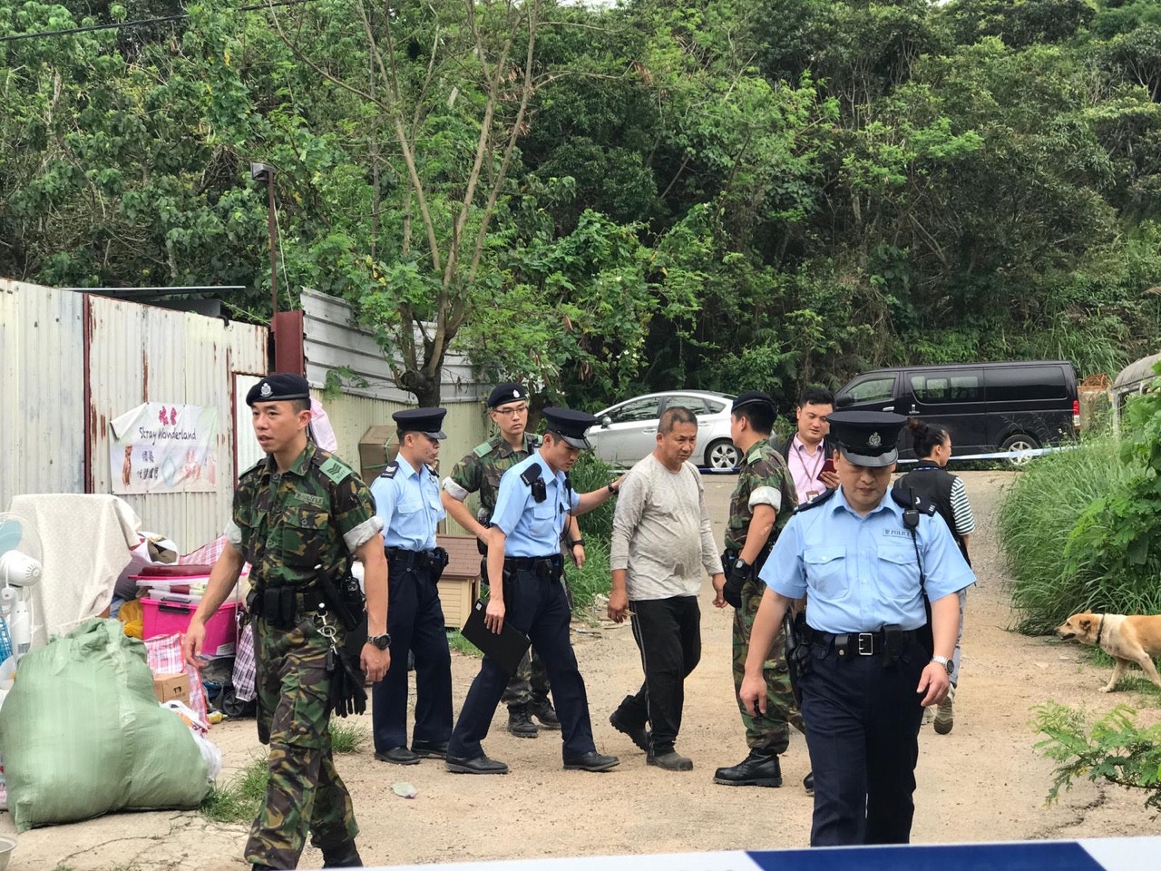 狗場主人鄭先生(白衣者)一度拒絕應門,最後因涉嫌損壞記者相機而被拉上警車。(義工林小姐提供) 狗場主人鄭先生(白衣者)一度拒絕應門,最後因涉嫌損壞記者相機而被拉上警車。(義工林小姐提供)