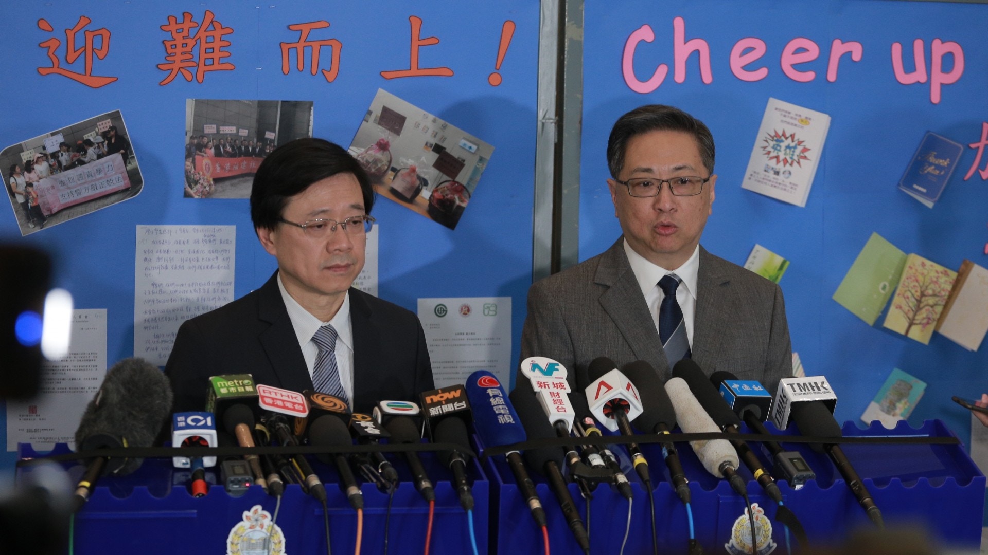 今日下午1時許，保安局局長李家超及警務處處長盧偉聰見記者，其身後的展覽板上貼有「迎難而上！」、「Cheer Up!」的字眼。（羅國輝攝）