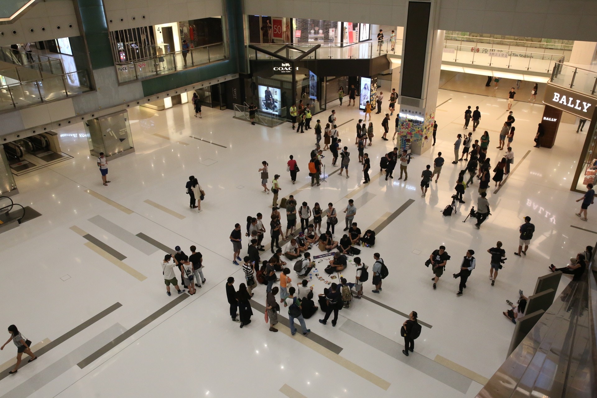 因為本浩翻開背包，沙田街坊逐漸圍在他身邊，在原本屬於公眾的廣場走道上，在兩排連鎖名牌店之間，通宵分享了對這場社會運動的想法。（陳永武攝）