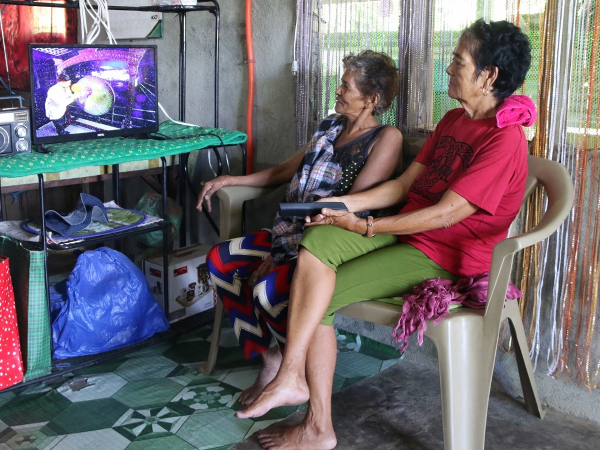 在菲律賓北部山區的巴利瓦特村,村長艾爾西·伊斯塔萬(右)在家中與朋友觀看電視節目。(新華社)