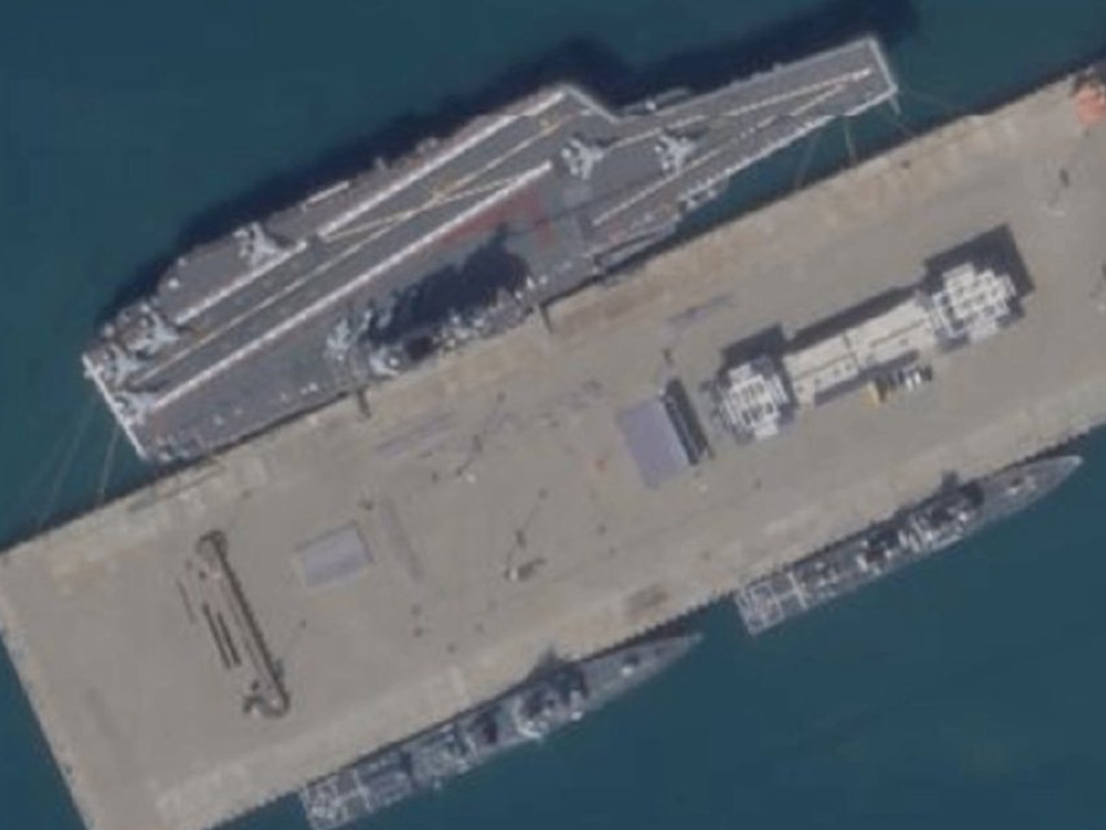 12月16日，衛星照顯示，位於三亞錦母角航母基地的棧橋上出現觀禮台，國產航母甲板上也出現紅地毯。（鼎盛軍事）