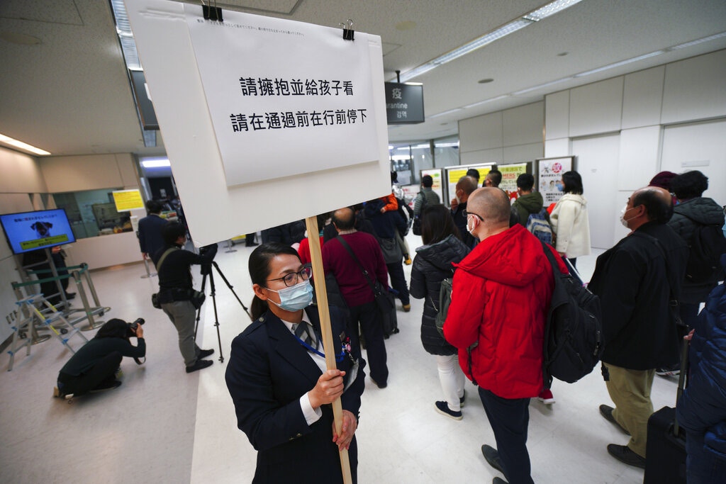 日本出现确诊个案，海关加强对入境旅客检查。图为1月23日成田机场一名检疫职员举起告示板，呼吁通过体温探测器的旅客配合他们的要求。（AP）
