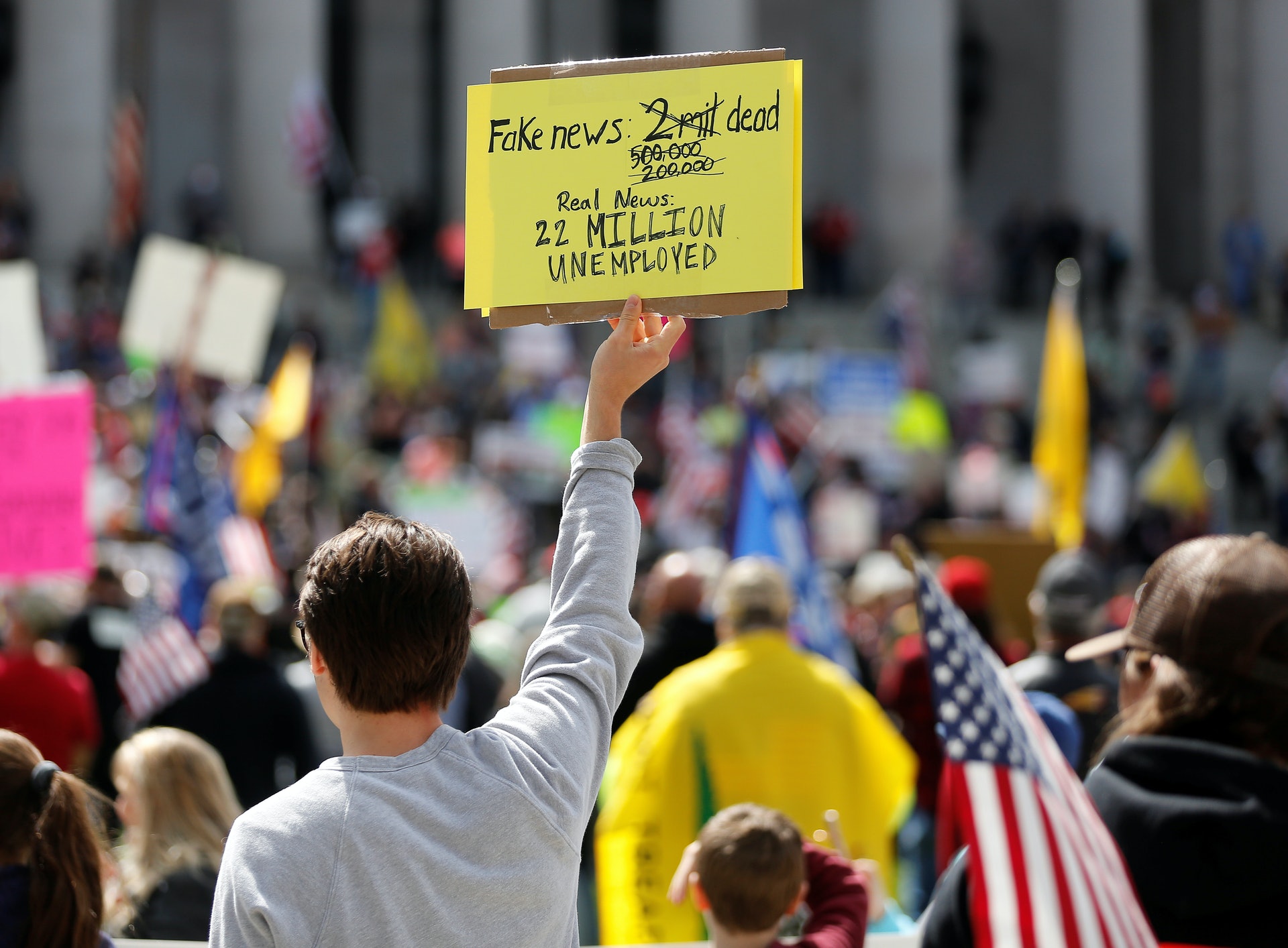 一名男子舉起標語，寫着「200萬人死是假新聞，真相是2000萬人失業」。（路透社）