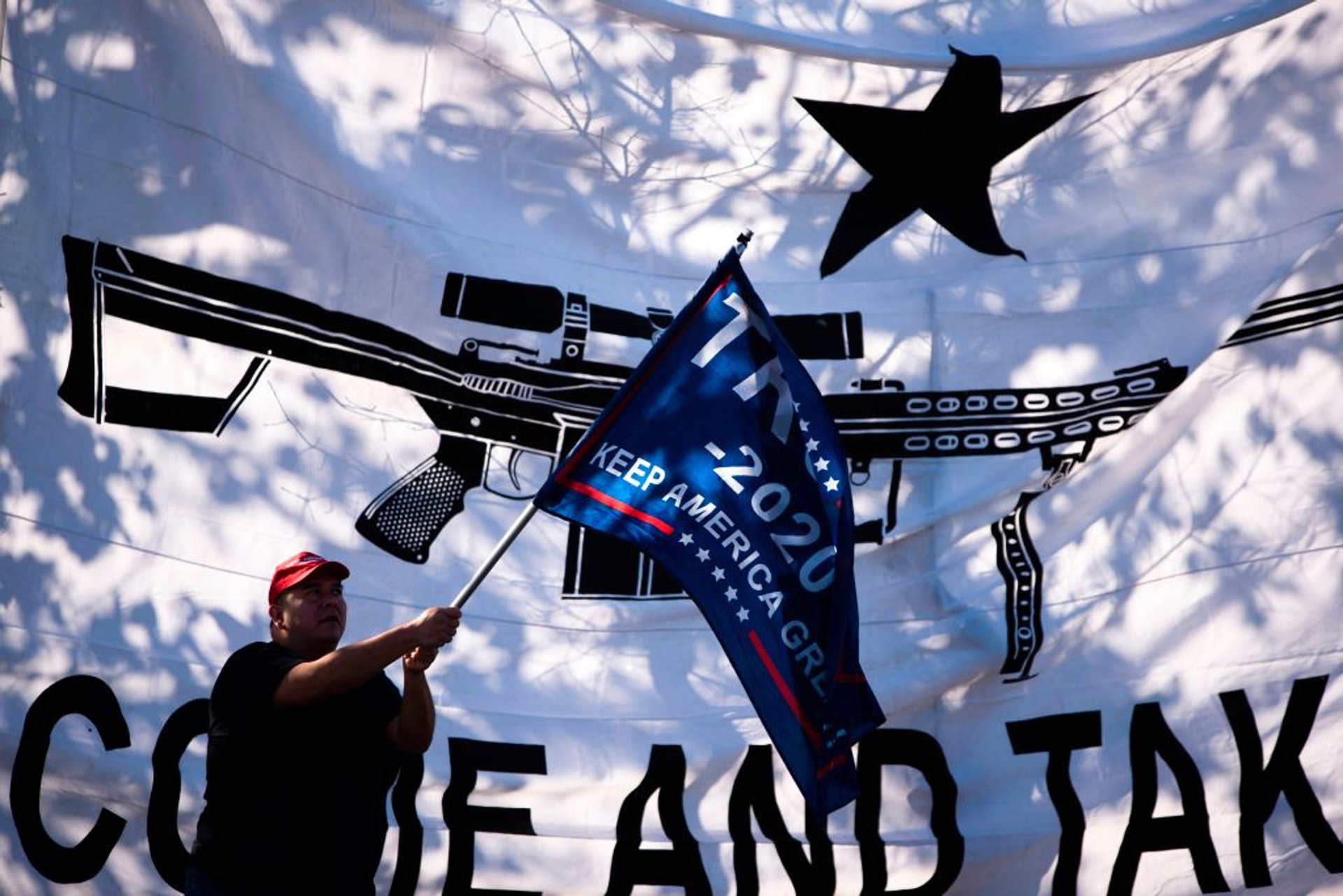 擁槍派出席反禁足示威，一名男子搖着「特朗普2020」的助選旗幟。（美聯社）