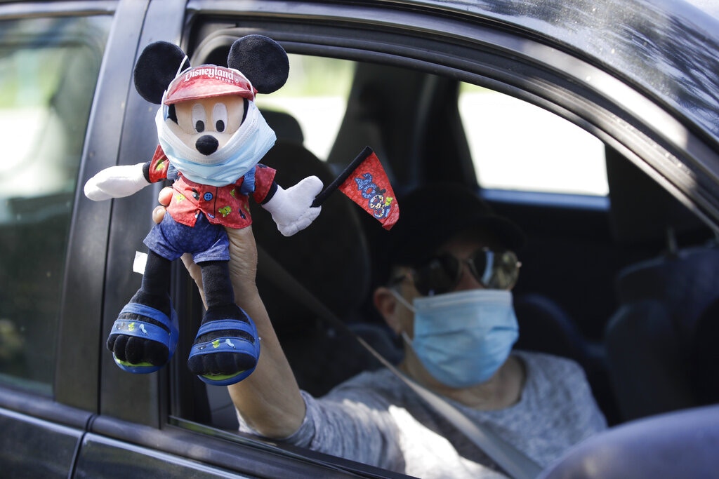 美國新冠肺炎疫情：加州阿納海姆6月27日有民眾駕車示威。圖為迪士尼一名員工在示威期間舉起一個戴口罩的戴上口罩的「米奇老鼠」玩偶。（AP）