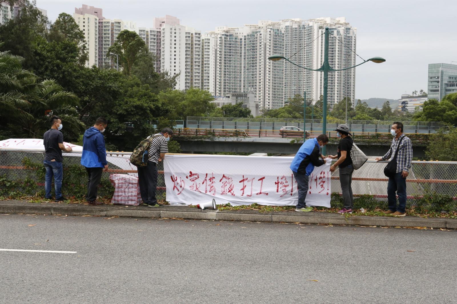 在場抗議的為釘板工人，在路邊鐵欄上掛起寫有「炒家借錢打工，慘！慘！慘！」的橫額。