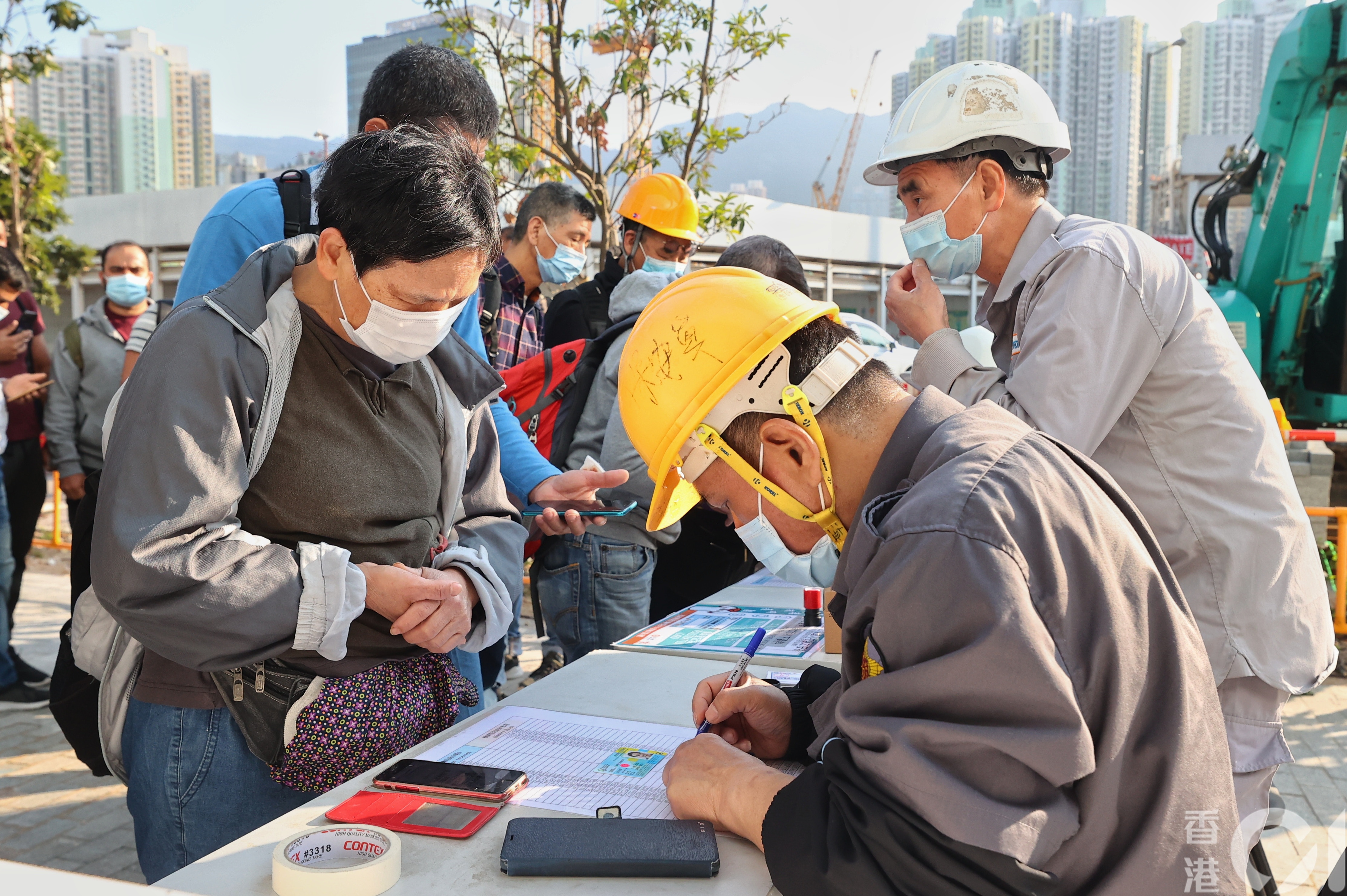 該地盤外約有3至4名保安員為排隊工人檢查陰性證明，並於名單上為工人標示已完成檢測。（張浩維攝）
