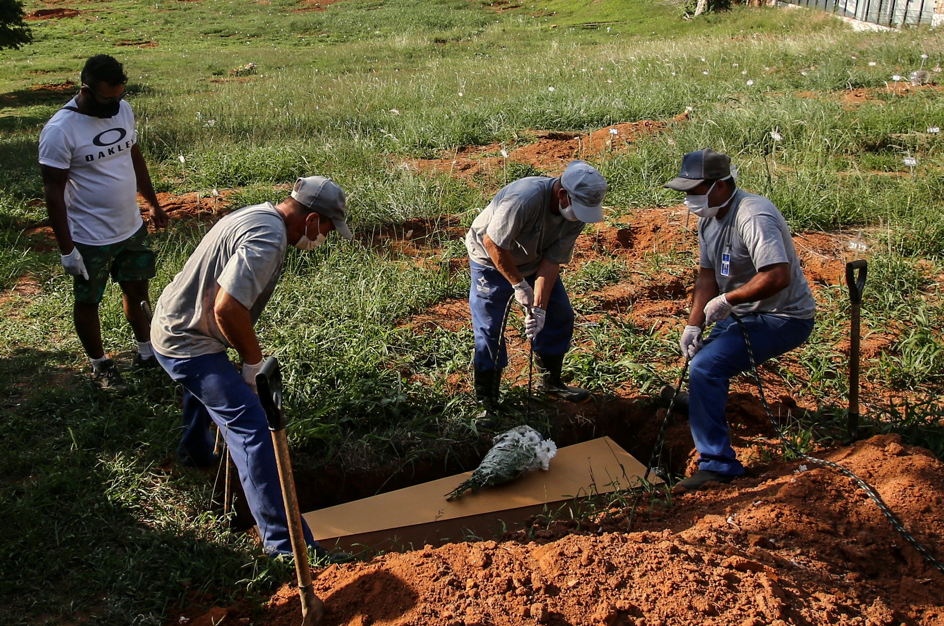 巴西新冠肺炎疫情：圖為4月6日巴西一名58歲的新冠肺炎死者在阿雷格里港一個墓地下葬，工作人員將其棺木放入墓穴。（Reuters）