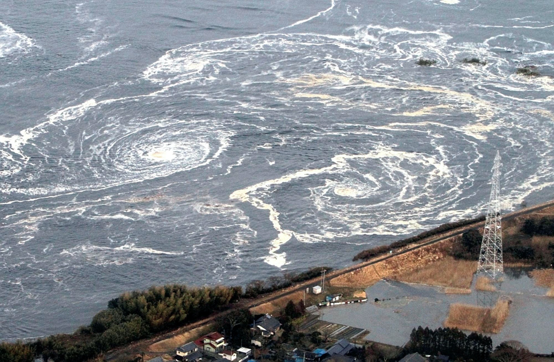2011年3月11日，日本福島縣，磐城市遭受海嘯沖擊，水面出現巨大旋渦。（Reuters）