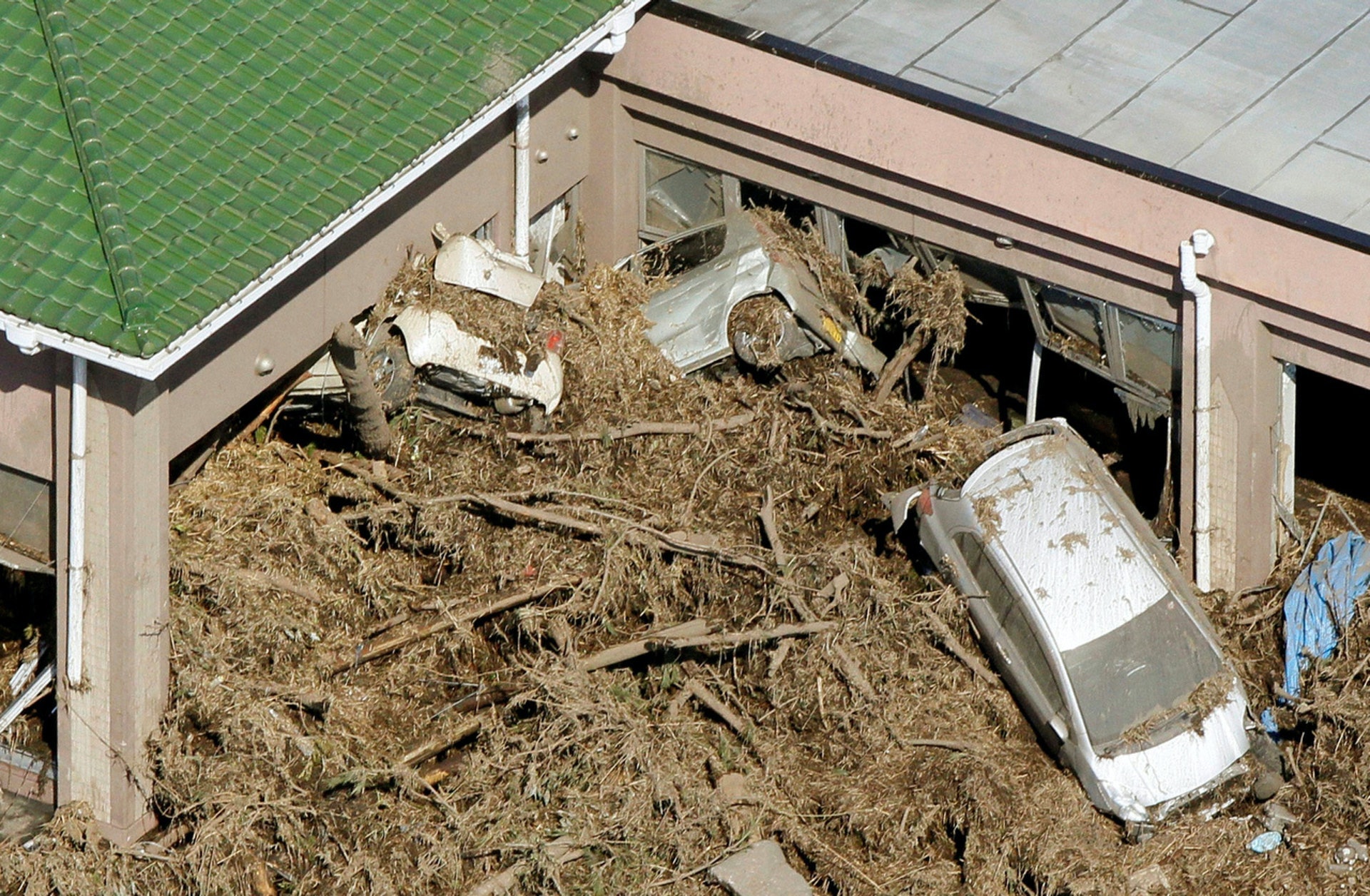2011年3月12日，日本福島縣，南相馬巿遭受海嘯沖擊，汽車、樹木被水沖走，堆積在建築物旁邊。（Reuters）