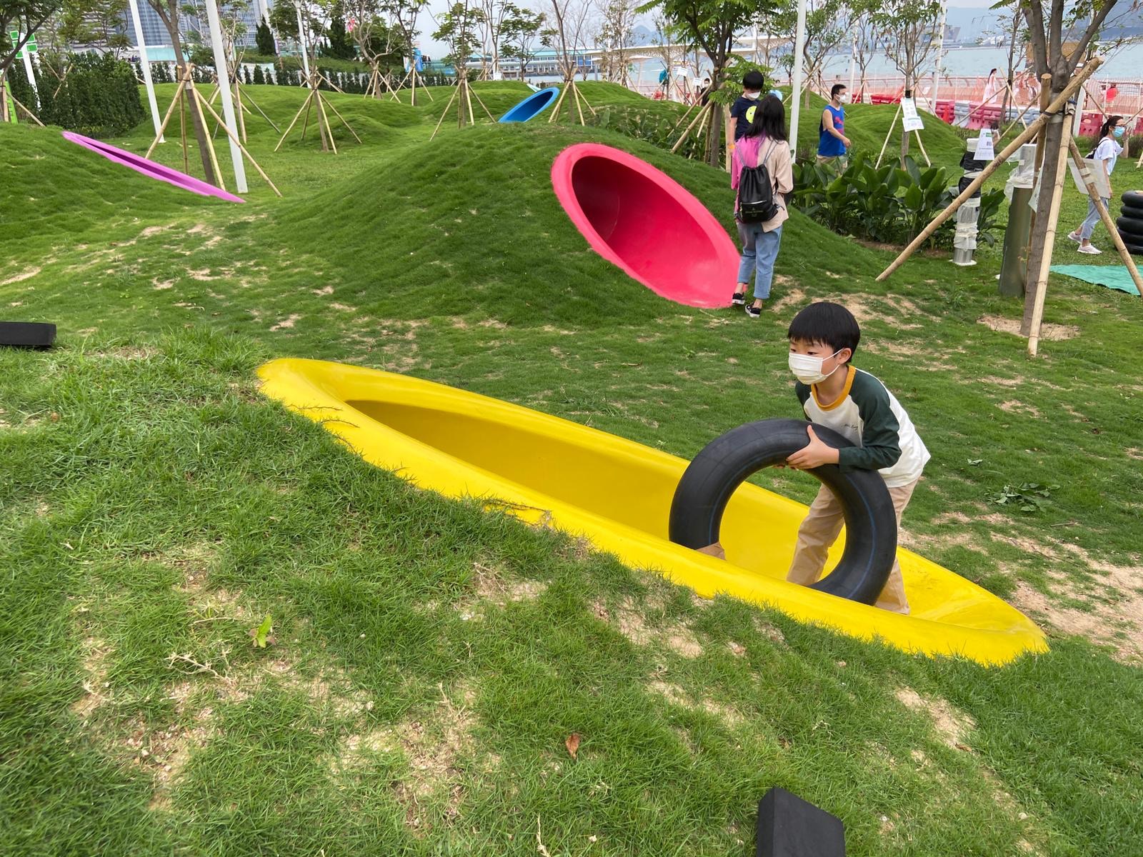 長廊靠近添馬公園的一端，設置了一個以「童樂園」為主題的活動區，藉着園境設計、高低起伏的草坪，配以色彩鮮艷的渠桶，於鬧市中營造天然風格的自由活動空間。（政府新聞網）