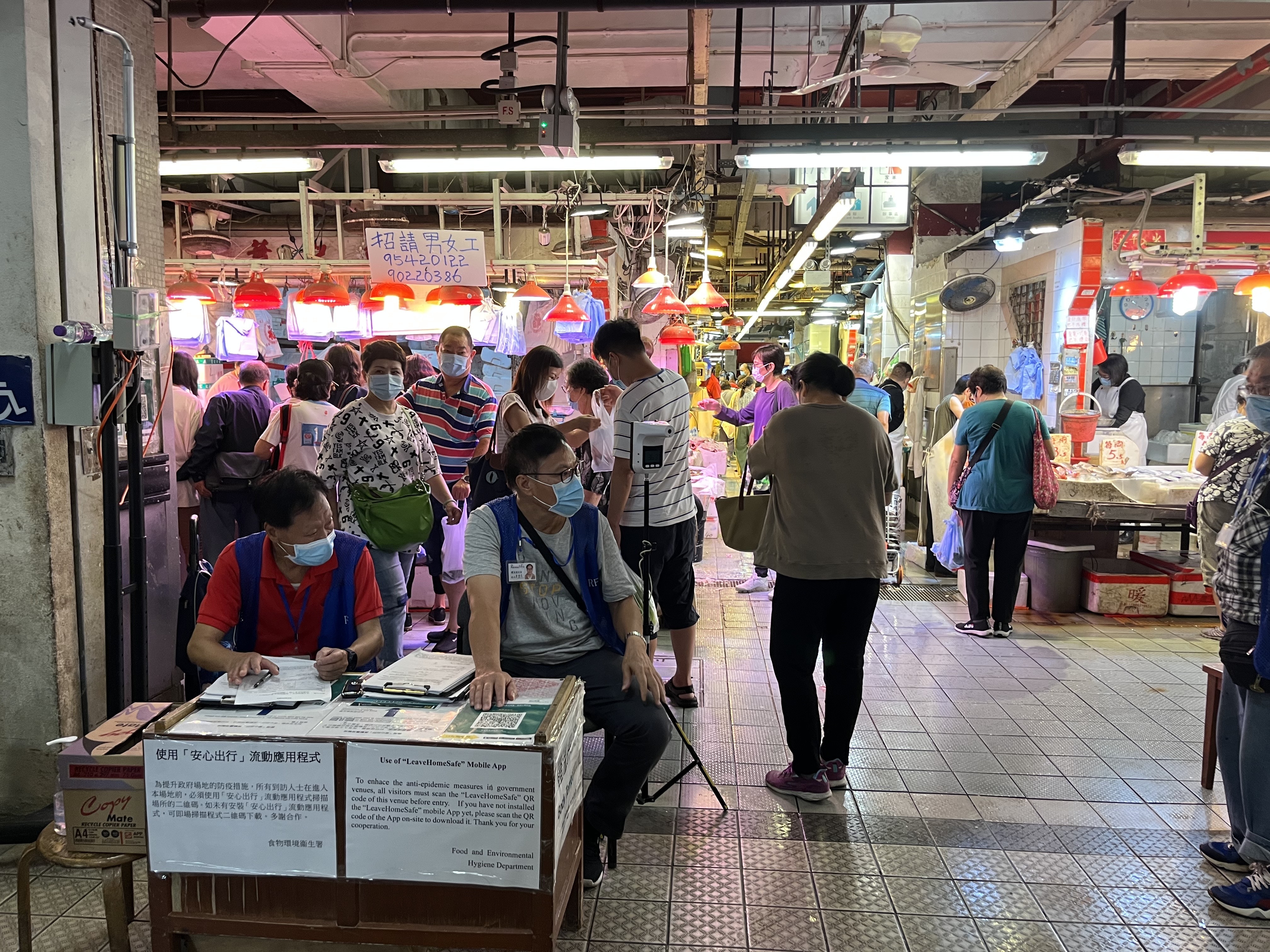 荃灣楊屋道街市多個出入口均有職員協助市民使用「安心出行」或填寫個人資料，亦有市民會將身份證遞上讓職員代為填寫，有長者表示，因為沒有智能手機而無法使用應用程式，慨嘆新措施麻煩又不便。（黎倩婷攝）