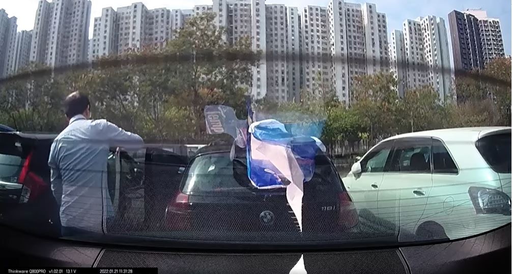 屯門1名男子被拍到不停以地氈拍打鄰車，藉此清理上面的碎石粒和灰塵。（fb「馬路的事討論區」影片截圖）