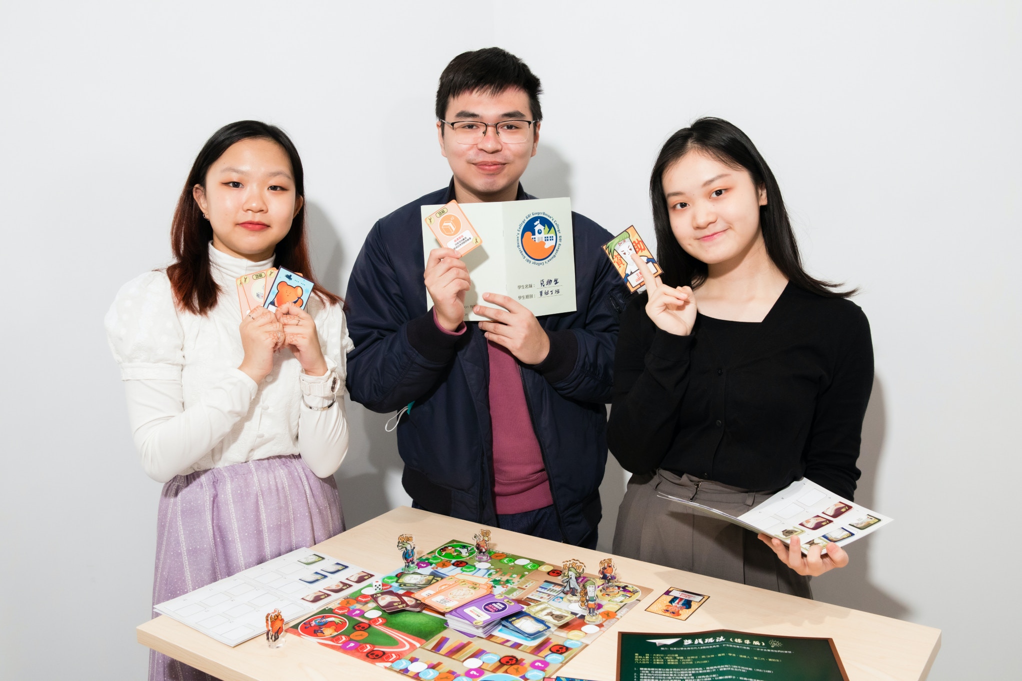 IVE公關及數碼傳訊高級文憑畢業生蘇泳暢（ Vincent） （ 中 ） 及吳樂童 （ Feliz）（左） 與 HKDI 插畫設計高級文憑畢業生梁念恩（Grace）（ 右 ）聯同其他同學一起設計桌上遊戲《薑蔥學園》，將快樂及正能量傳遞予年輕人。（職業訓練局提供圖片）