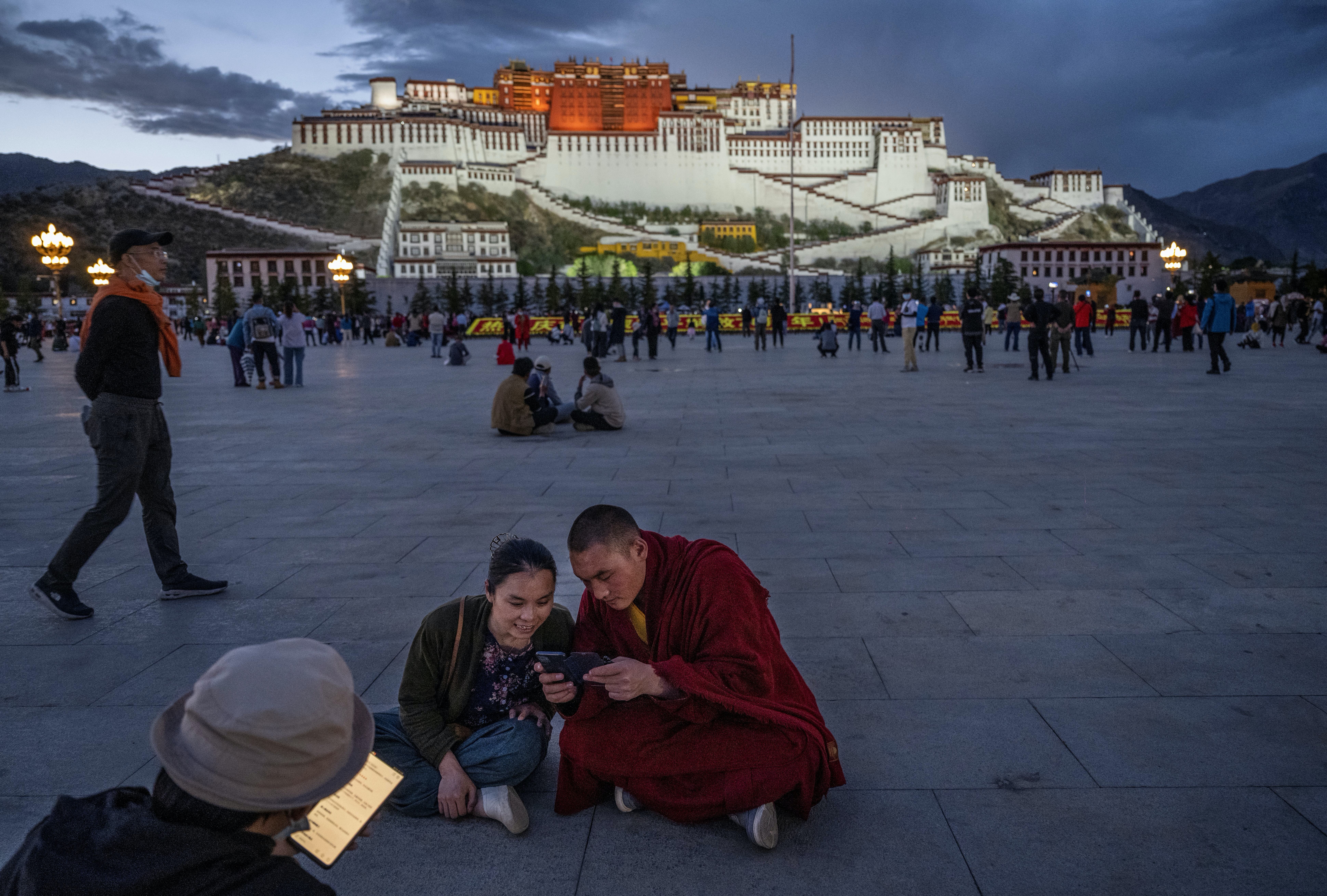 2021年6月1日，西藏自治區拉薩市，一名藏傳佛教僧侶和一名婦女坐在布達拉宮前看手機。（Getty Images）