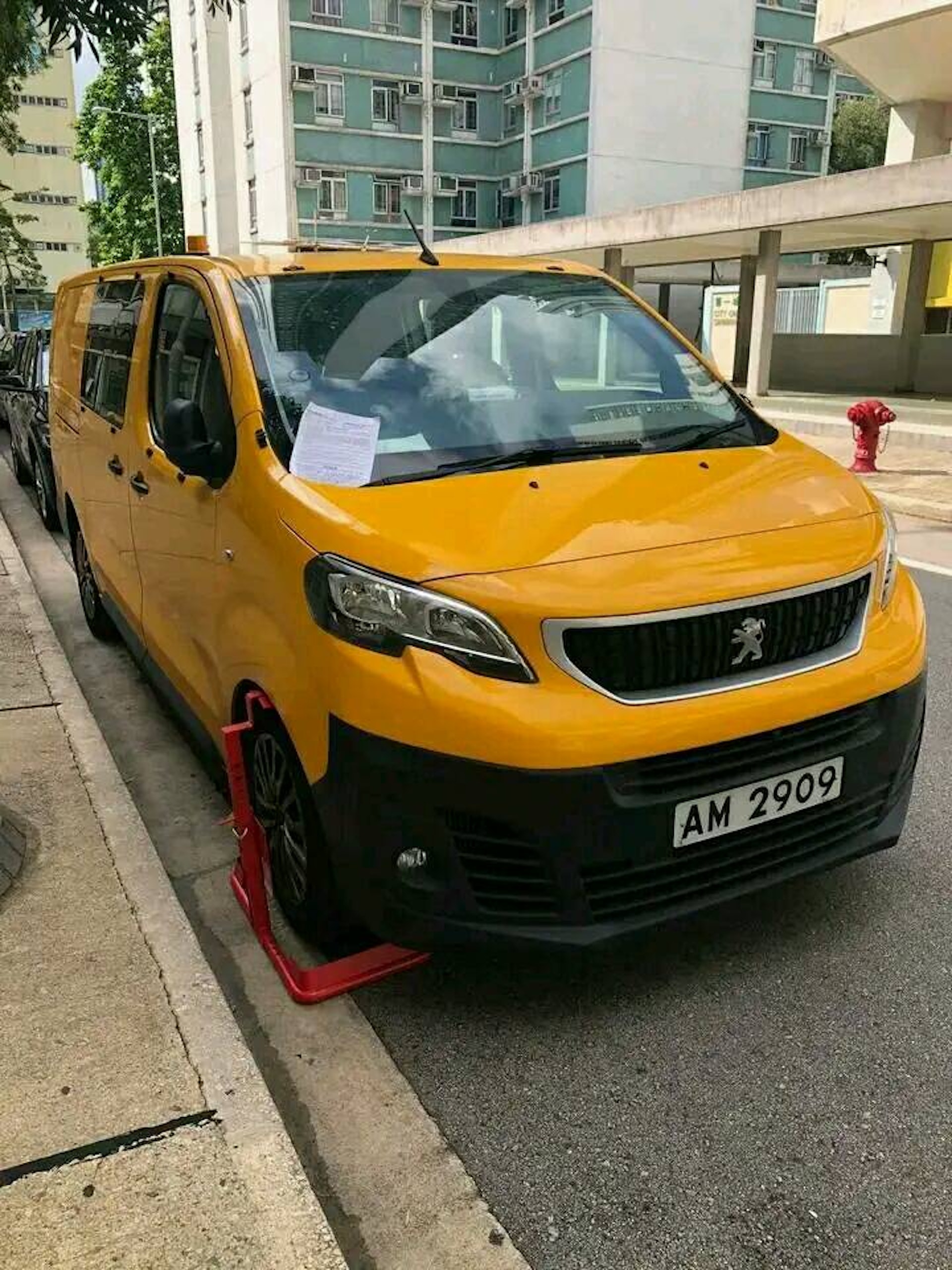有網民拍到1輛AM車牌的黃色客貨車,停泊在第一城屋苑範圍內,右前轆則被上鎖,而車頭擋風玻璃則夾有1份文件。(FB「的士司機資訊網 Taxi」圖片) 有網民拍到1輛AM車牌的黃色客貨車,停泊在第一城屋苑範圍內,右前轆則被上鎖,而車頭擋風玻璃則夾有1份文件。(FB「的士司機資訊網 Taxi」圖片)