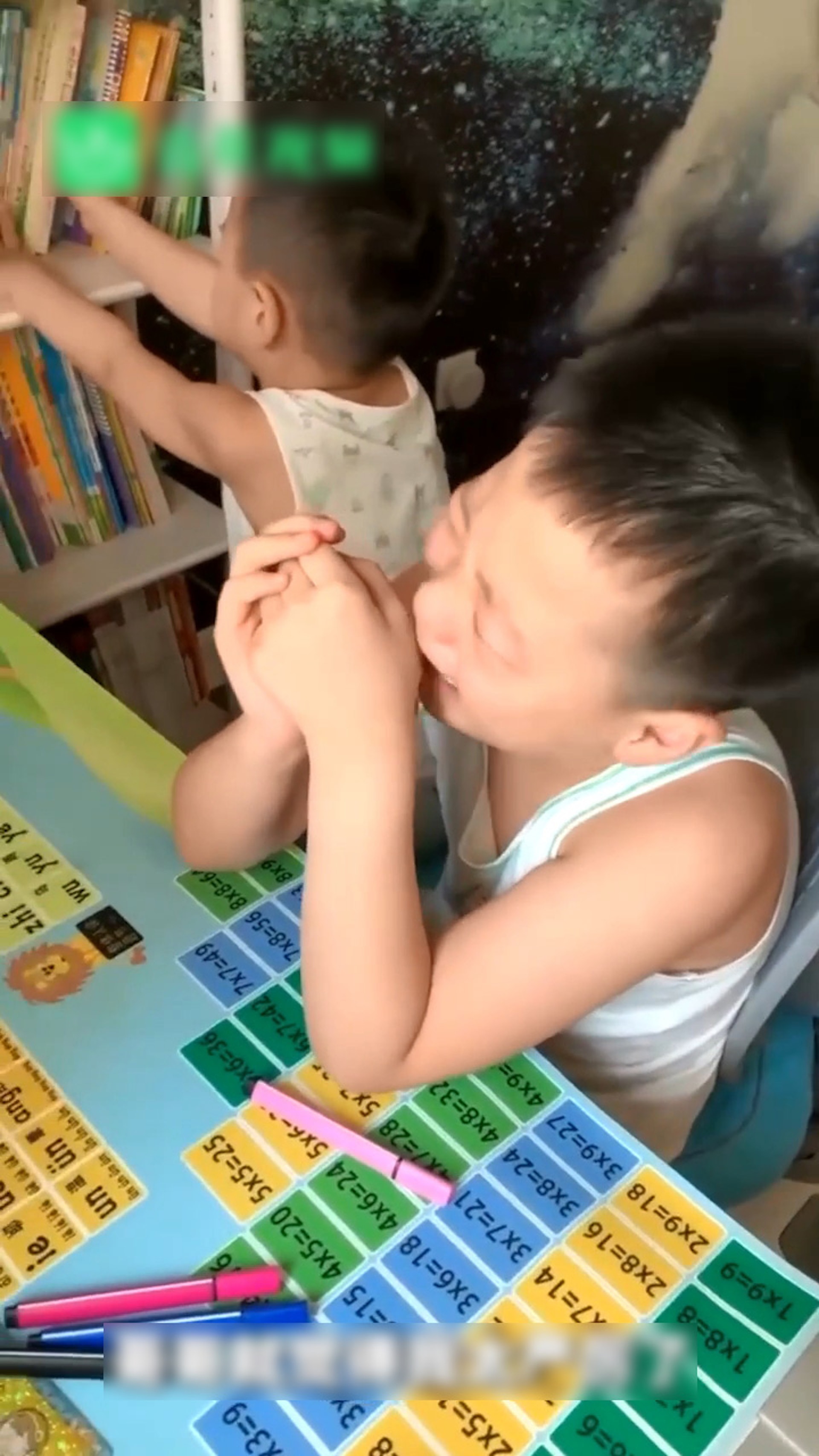 哥哥失聲痛哭，弟弟玩弄旁邊的書架。（微博影片截圖）