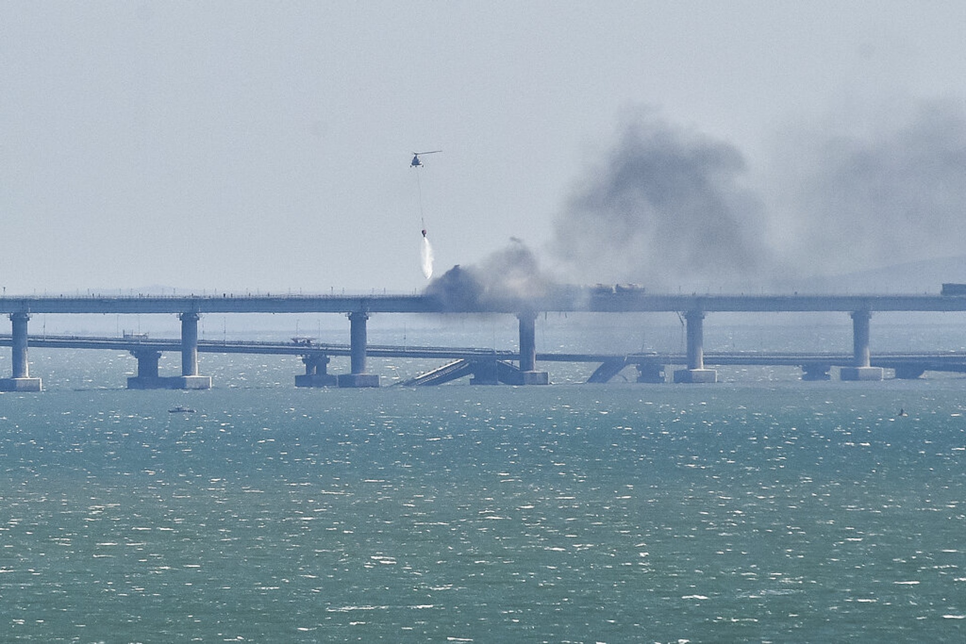 克里米亞大橋爆炸:俄羅斯國家反恐委員會稱,2022年10月8日清晨6時過後,一輛來自塔曼半島方向的貨櫃車,在克里米亞大橋(又稱刻赤大橋)的公路橋發生爆炸,導致載有燃油的火車7節車箱起火,公路橋2處地方部份塌陷。圖為事發後一部直升機飛到大橋上方救火。(AP) 克里米亞大橋爆炸:俄羅斯國家反恐委員會稱,2022年10月8日清晨6時過後,一輛來自塔曼半島方向的貨櫃車,在克里米亞大橋(又稱刻赤大橋)的公路橋發生爆炸,導致載有燃油的火車7節車箱起火,公路橋2處地方部份塌陷。圖為事發後一部直升機飛到大橋上方救火。(AP)