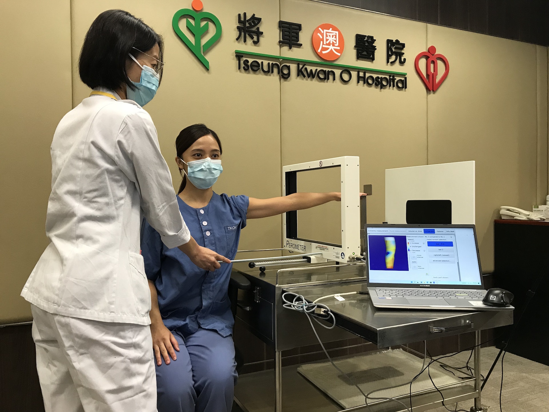 蔡惠榮與另一名護士，用紅外線三維測量儀檢查病人。可見醫護可拉動一方形的掃瞄器，如「影印機」掃過病人手臂。(梁晉穎攝)