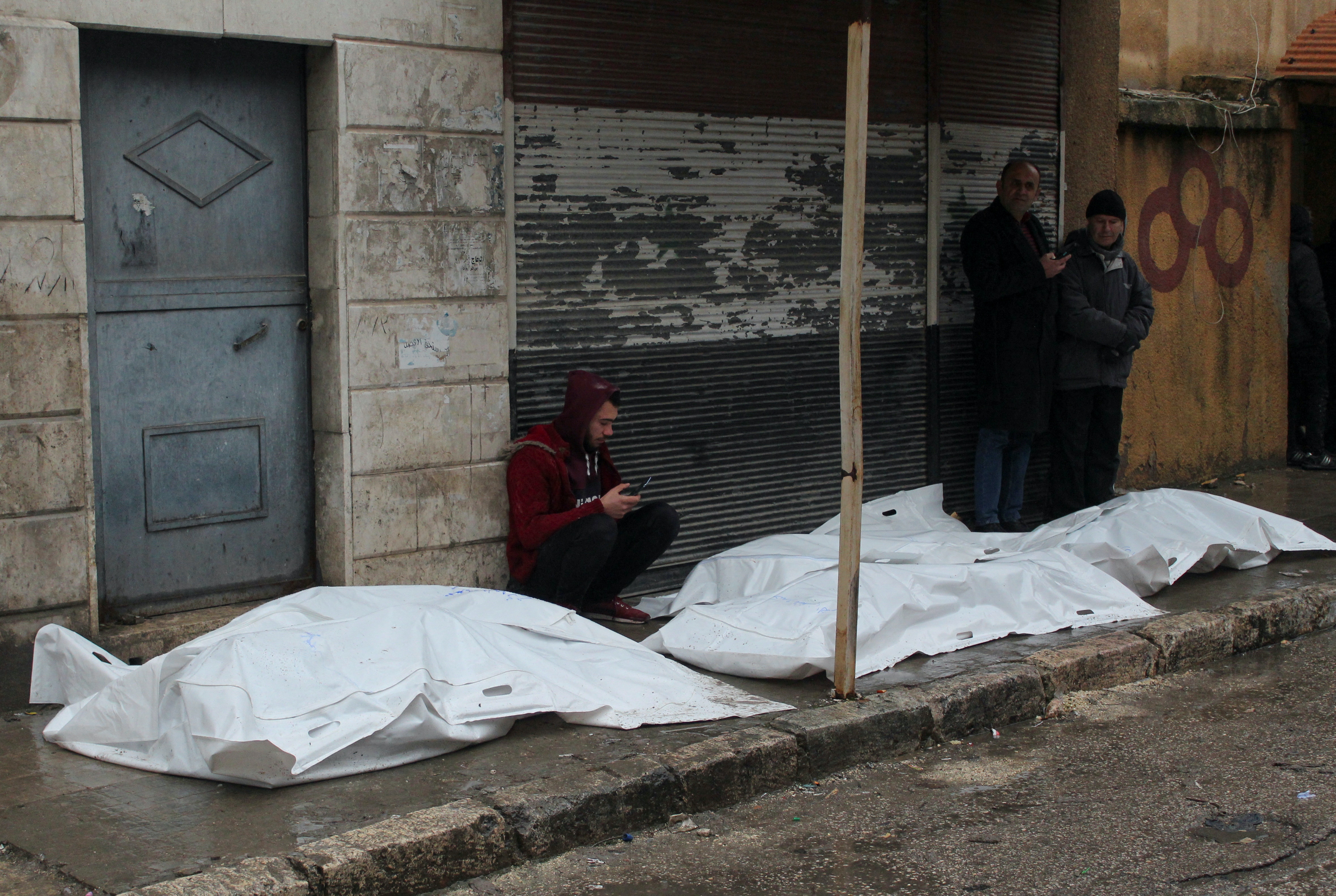 2023年2月6日，地震發生後，敘利亞阿勒頗一名男子坐在躺在地上的袋裝死屍旁。（Reuters）