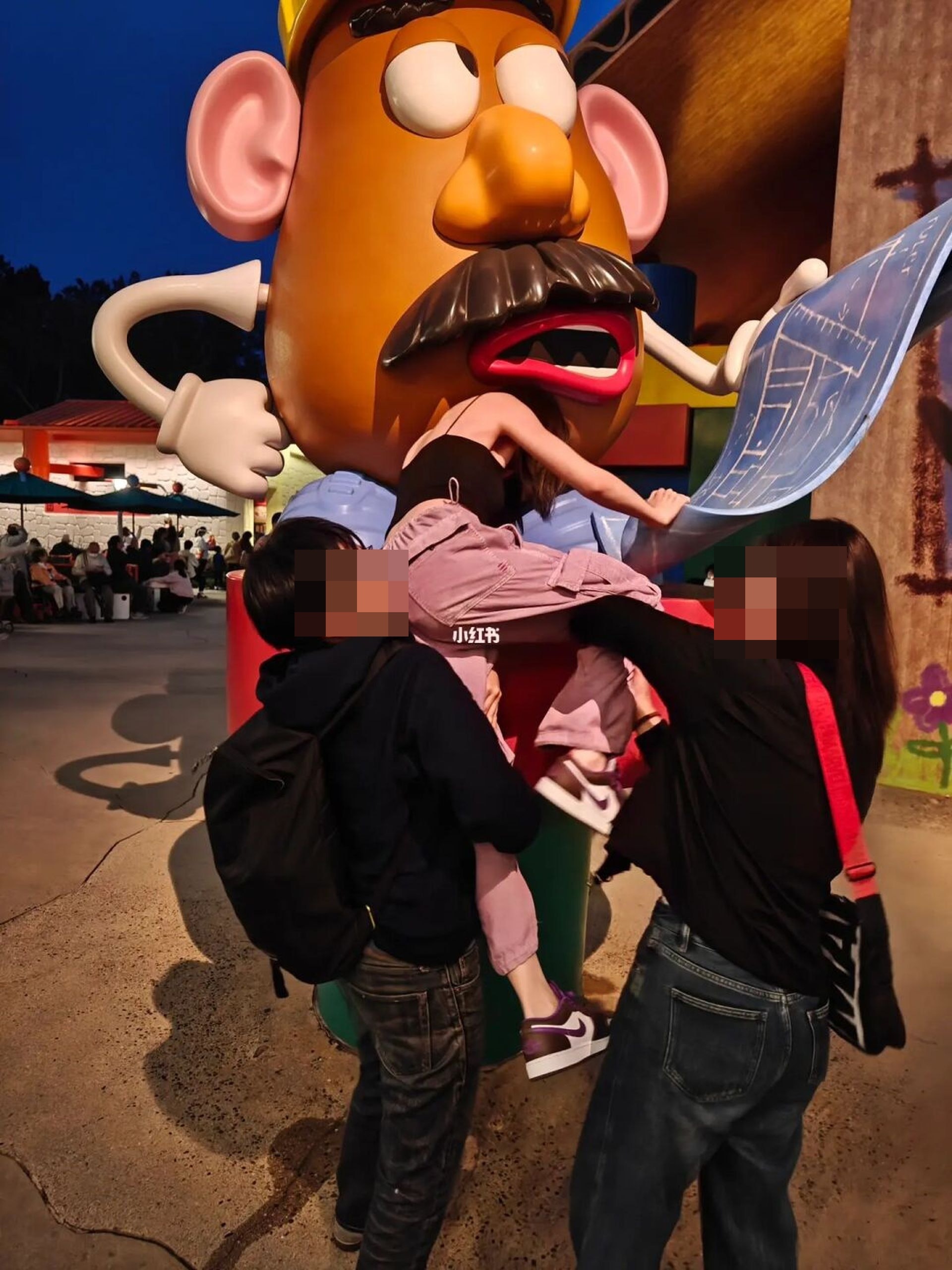 女子與其2名友人合力，爬上迪士尼園區內的一個「薯蛋頭先生」大型展品，欲坐在上面打卡。（截自小紅書）