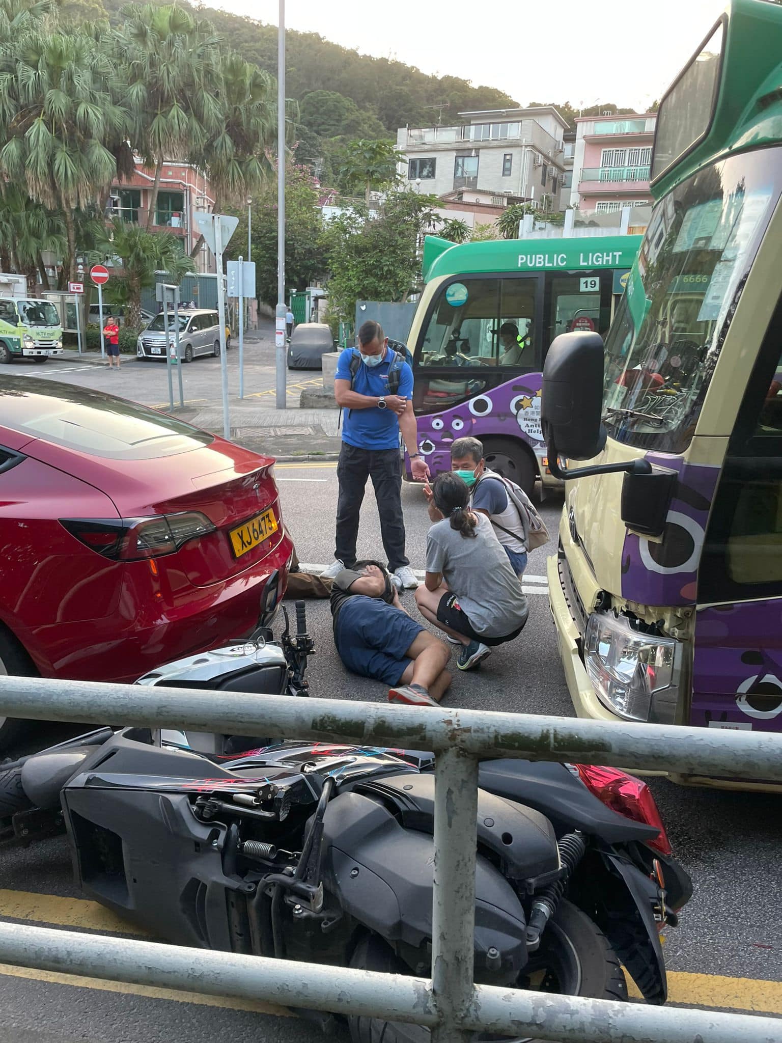 西貢公路三車相撞，見到電單車翻側，現場有兩名男子受傷倒地，途人蹲下視察傷者情況。 （fb群組「車cam L（香港群組）」圖片）