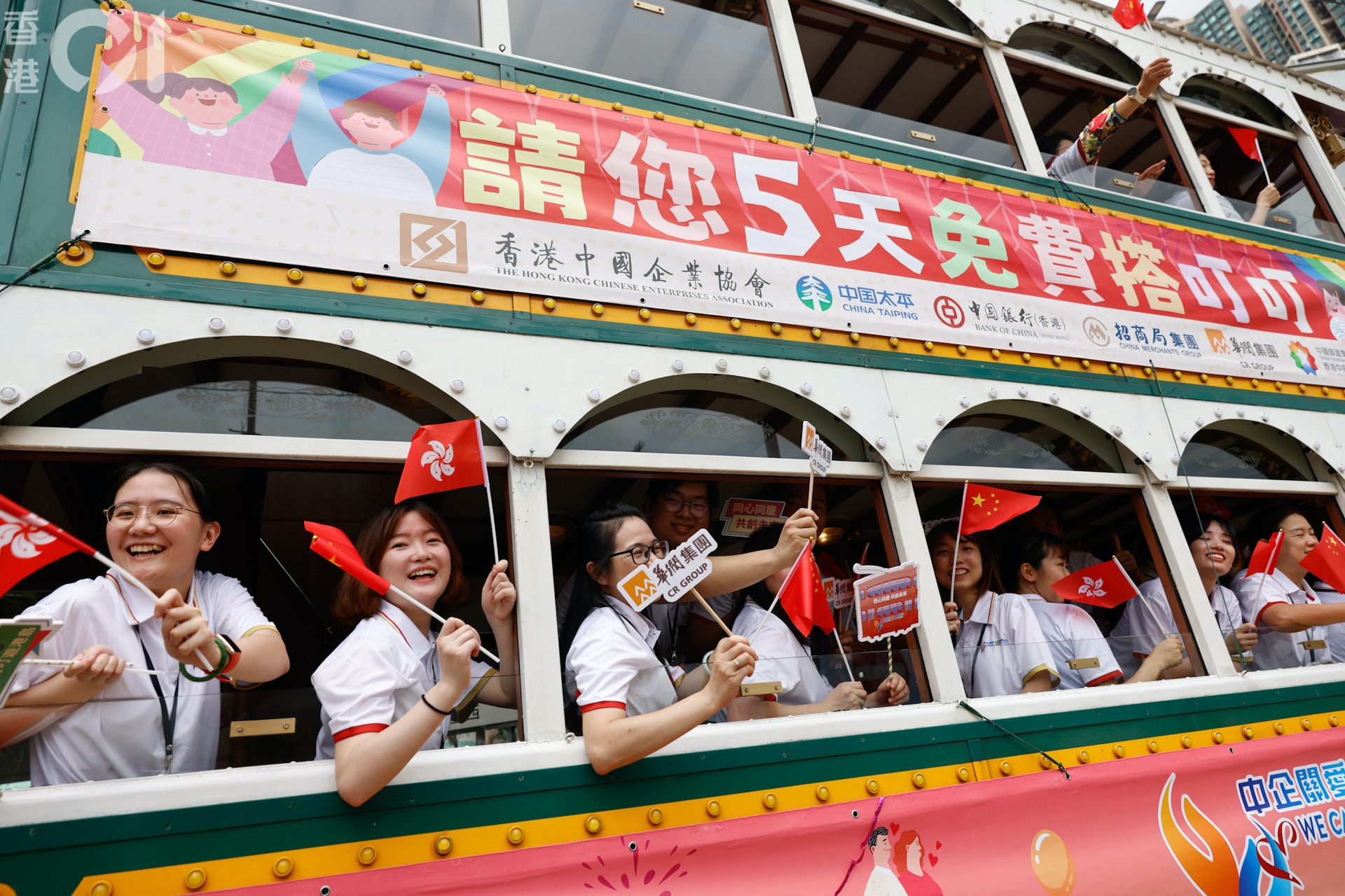 7月1日，免費乘搭香港電車活動，出席啟動禮的參加者揮舞國旗區旗登上電車。（羅國輝攝）