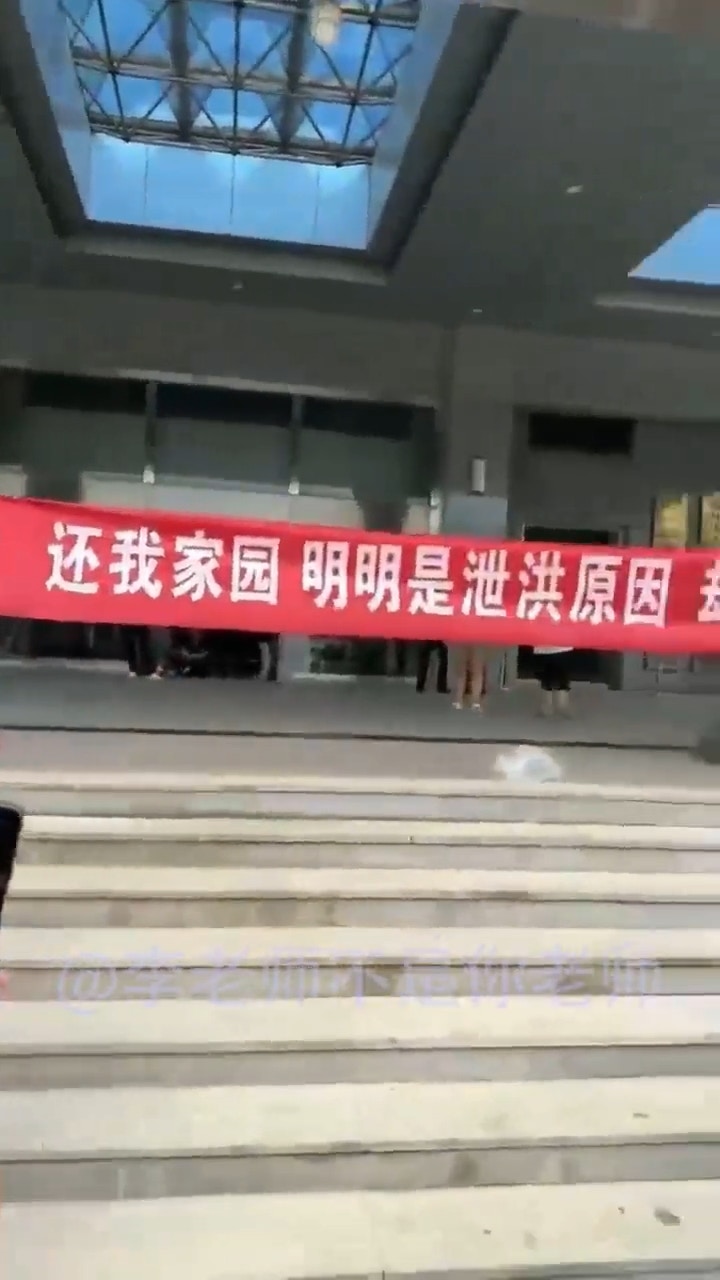 多名霸州市災民4日前往當地政府大樓進行抗議，在現場高舉紅色橫幅布條：「還我家園，明明是泄洪原因，卻說降雨所致」。（影片截圖）