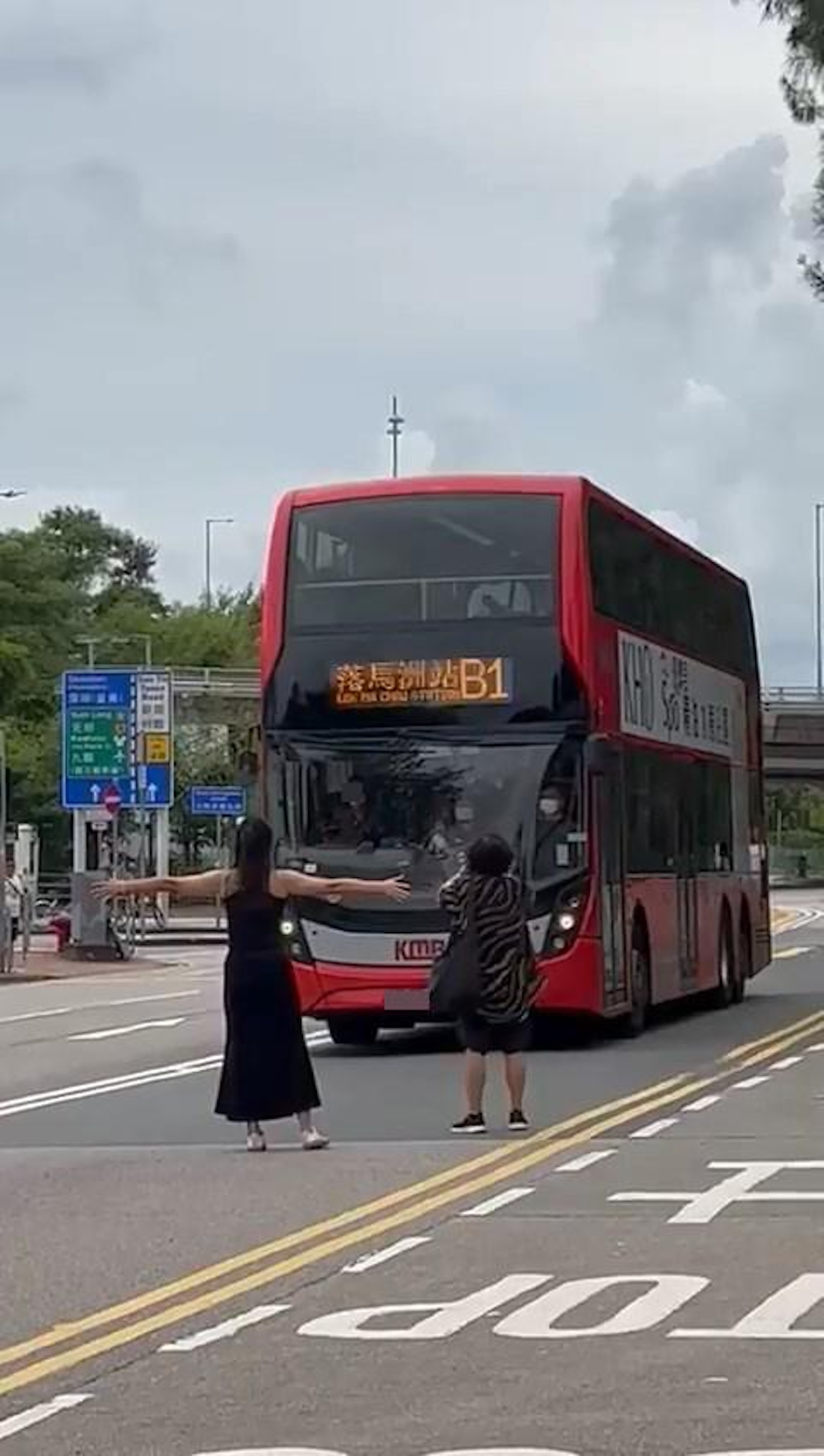 穿黑色背心長裙的盛裝女子,與另1名大媽正站在馬路巴士前方,其中長裙女大字形展開雙手攔住巴士,大媽則對着巴士「手指指」疑似在指罵車長。(影片截圖) 穿黑色背心長裙的盛裝女子,與另1名大媽正站在馬路巴士前方,其中長裙女大字形展開雙手攔住巴士,大媽則對着巴士「手指指」疑似在指罵車長。(影片截圖)