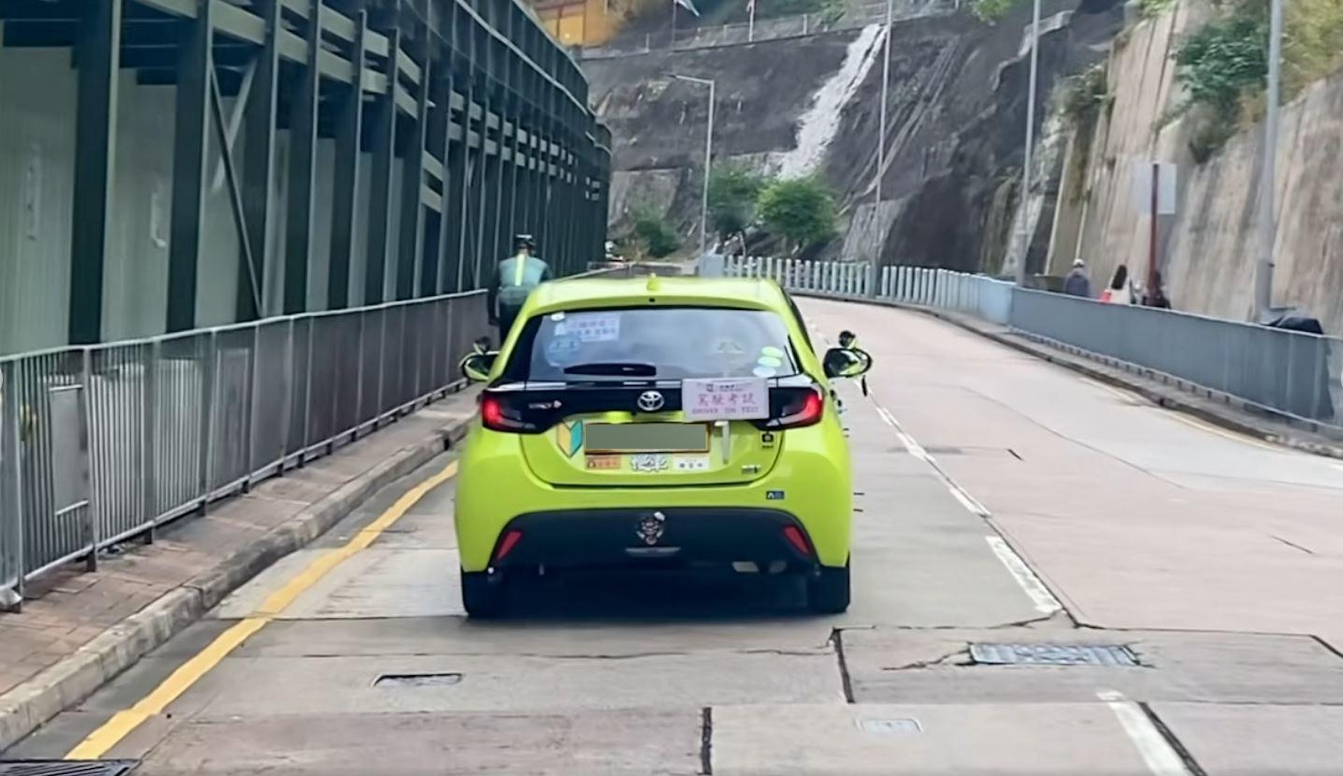 網上流傳影片,顯示1名私家車駕駛考試的考生在一上斜路段「龜速」前進,原因是前方有1名男子正踩單車,考生全程沒有爬頭。(facebook影片截圖)