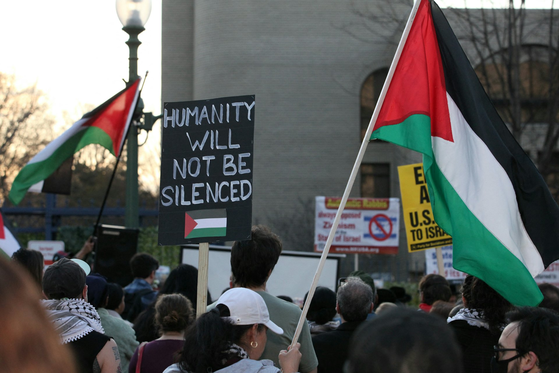 2024年2月26日，美國空軍飛行員布什內爾在以色列駐華盛頓大使館前自焚身亡翌日，人們在華盛頓出席悼念會。現場有人舉起標語，寫道：「人性將不會被噤聲」。（Reuters）