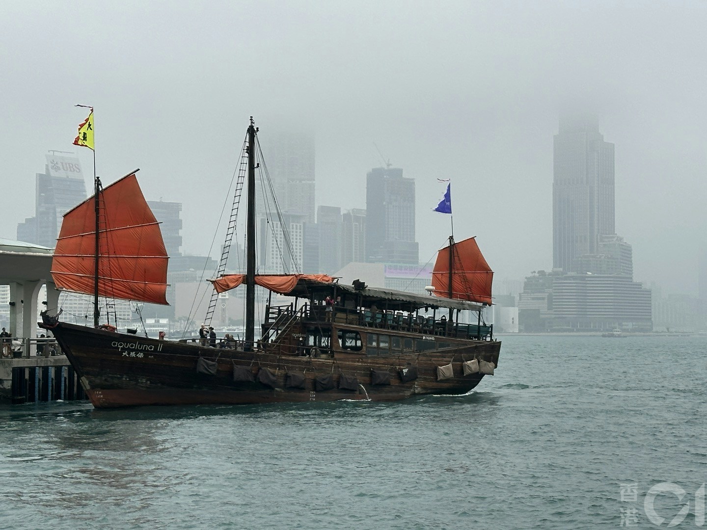 3月16日潮湿有雾，维港一片灰蒙蒙，在中环海滨望向对岸，可见部份大厦高层被云雾遮蔽，海上的红色帆船份外抢眼。（倪清江摄）