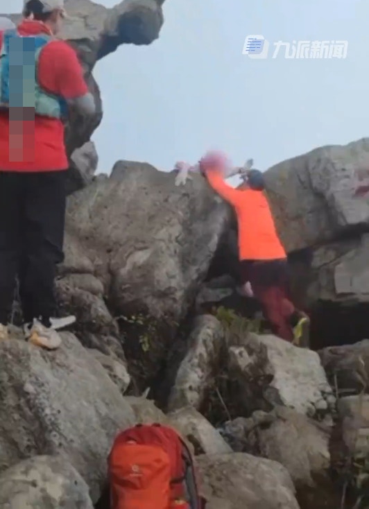 一名游客在龟仙石打卡拍照时双脚腾空，仅用双手攀住石头，落地时不慎跌倒。（九派新闻）