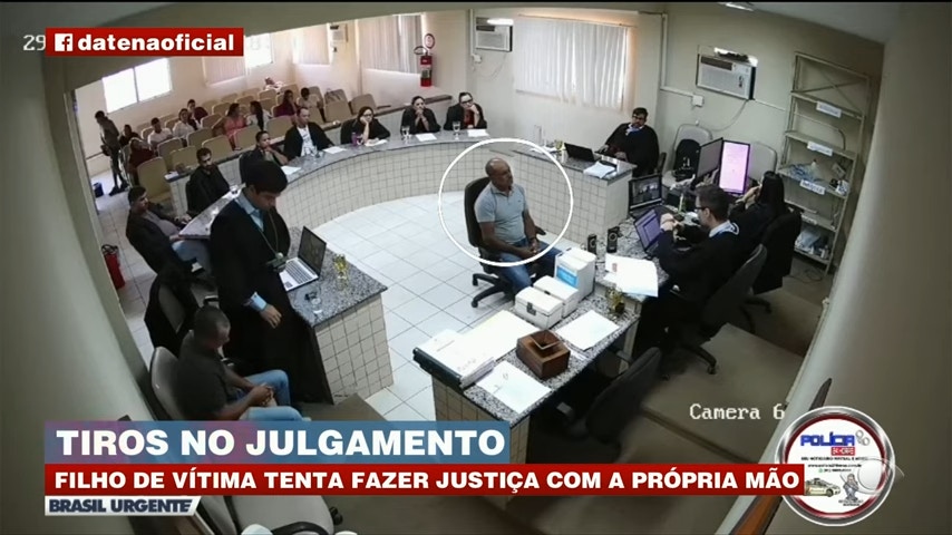 巴西一名男子的父亲遭人枪杀身亡，为了替父亲报仇，他在开庭时突然掏出预藏的枪枝，朝被告（白圈者）开了6枪，造成混乱。（YouTube截图 / @Brasil Urgente）