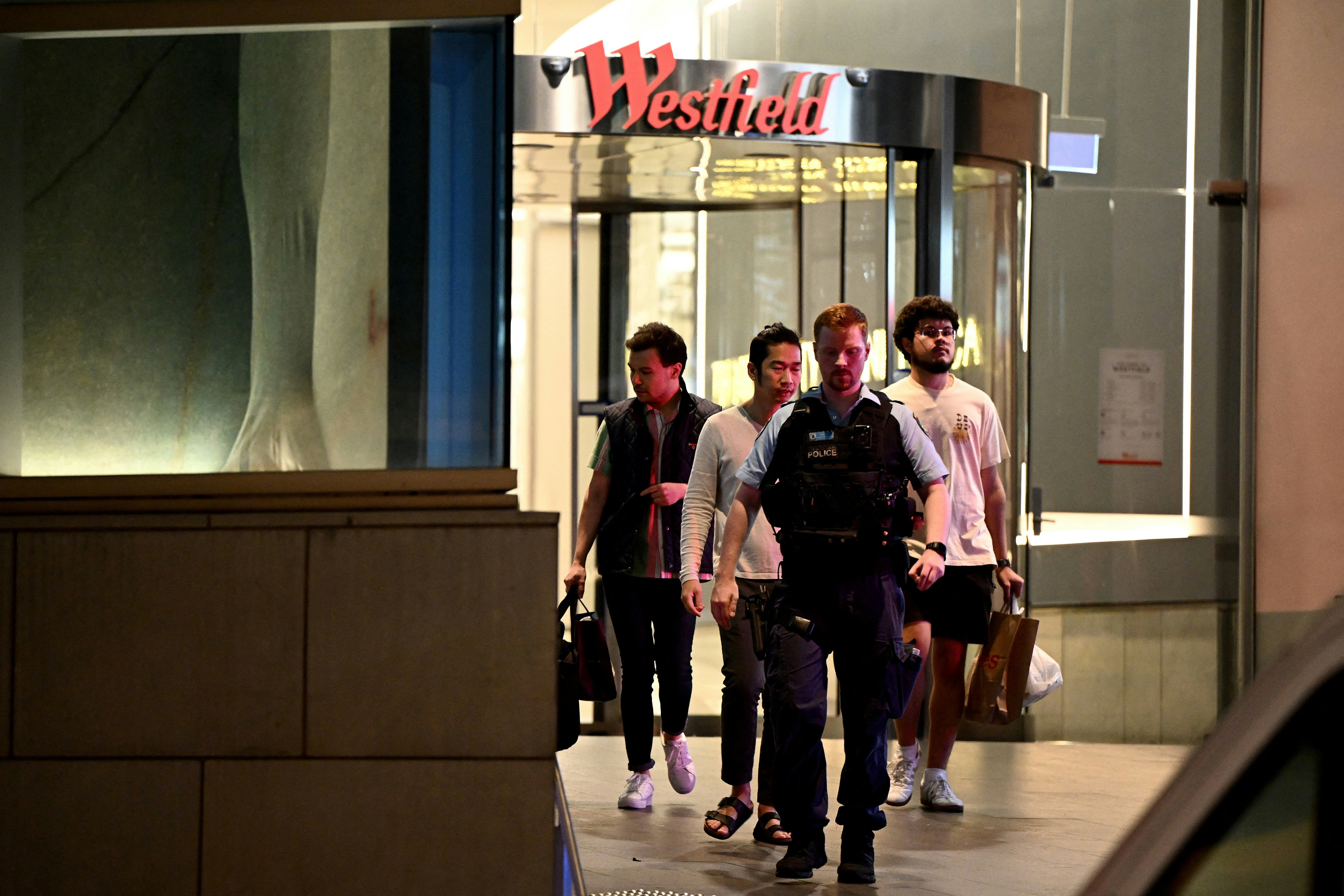 位于澳洲悉尼东部的购物中心Westfield Bondi Junction在2024年4月13日多人被人用刀刺伤，数人死亡。涉案男疑犯被女警开枪击毙。图为案发后身在商场内的途人在警员陪同下离开。（Reuters）