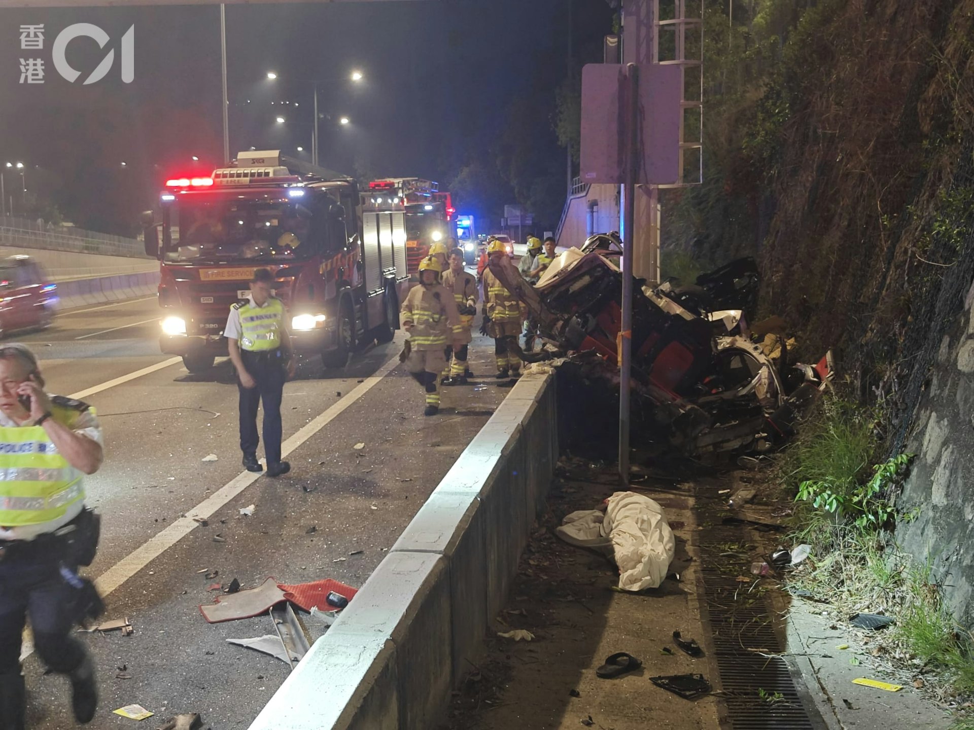 涉事私家車懷疑先撞龍門架,再飛出路壆外,全車盡毀。救護人員用白布遮蔽死者遺體。 涉事私家車懷疑先撞龍門架,再飛出路壆外,全車盡毀。救護人員用白布遮蔽死者遺體。