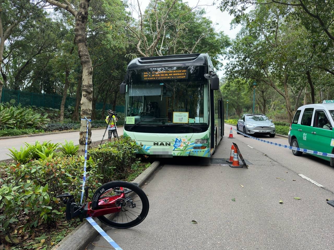 涉事旅遊巴半邊車身剷上路中花槽石壆，單車倒在其前方。（林澤鋒攝）