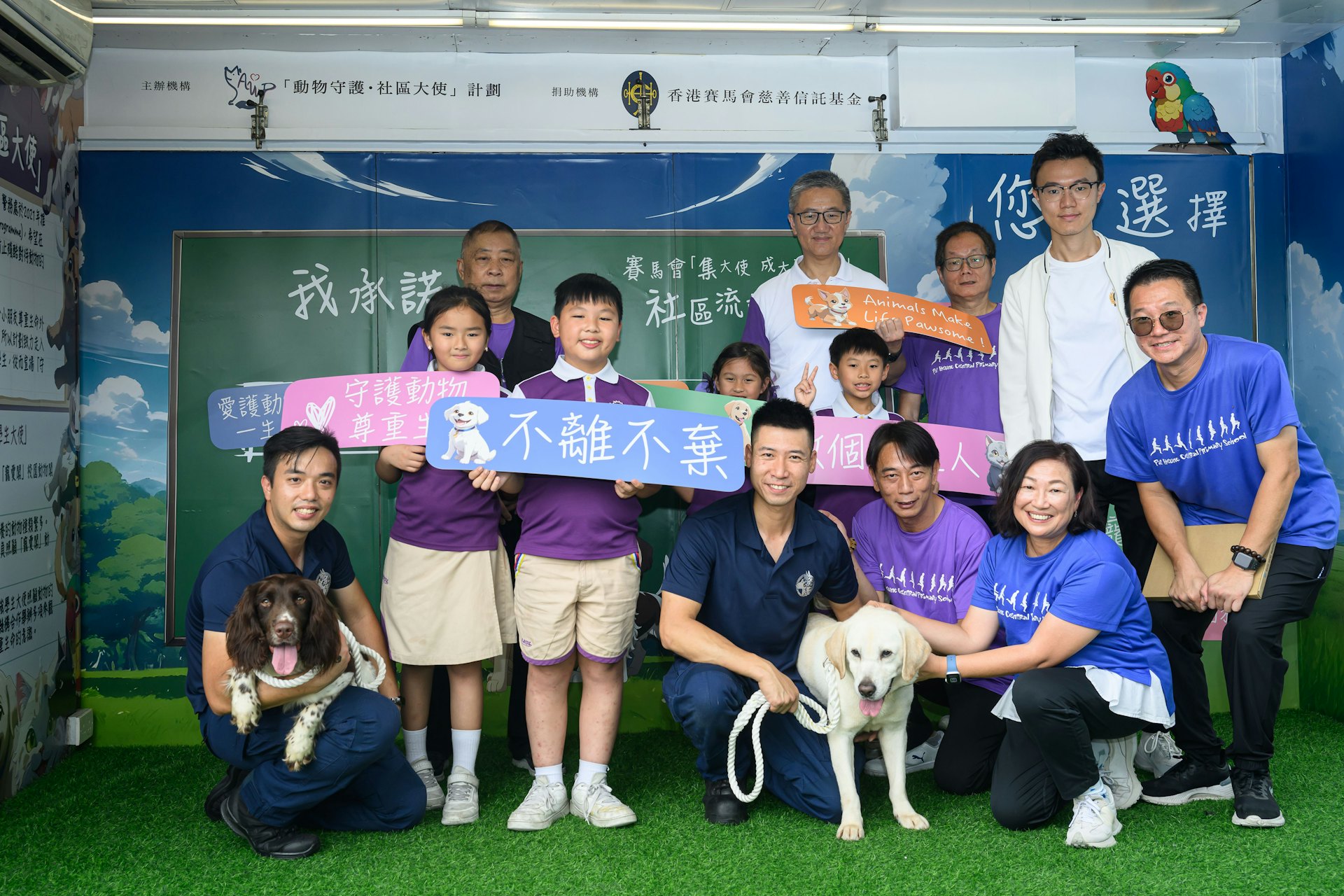 警方周五(26日)於八鄉中心小學舉行社區流動教室2.0」計劃啓動儀式,主禮嘉賓警務處處長蕭澤頤與學生一同和其中兩隻「守護之星」警犬合照。(警方提供圖片) 警方周五(26日)於八鄉中心小學舉行社區流動教室2.0」計劃啓動儀式,主禮嘉賓警務處處長蕭澤頤與學生一同和其中兩隻「守護之星」警犬合照。(警方提供圖片)