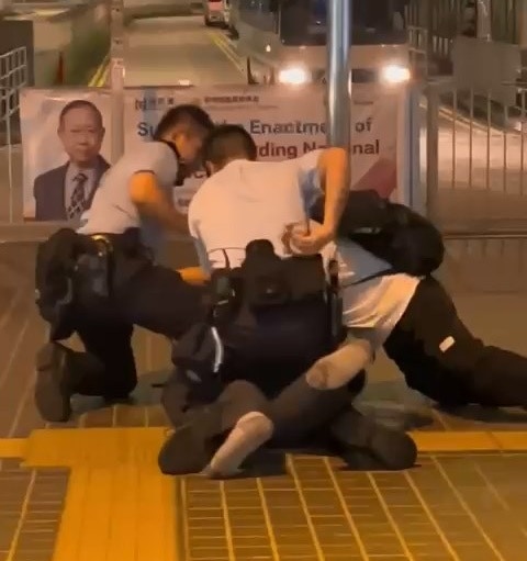 一名身材壮硕的男子，在屯门港铁兆康站外，被警员等人揿于地上制服；当时壮汉两只鞋踪杳，仅穿袜子。（网上影片截图）