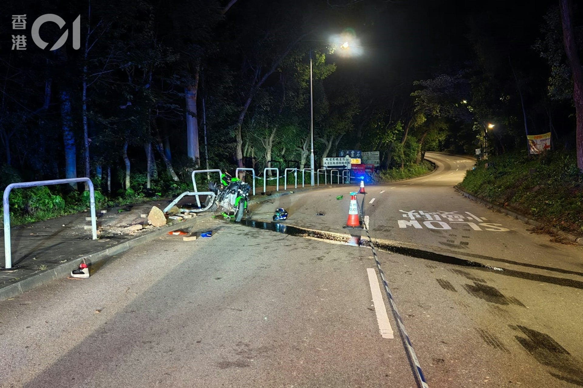 電單車撞毀路邊鐵欄,欄杆變型、地磚被撬起。現場留下相信屬於死傷者的頭盔及鞋,大量機油則沿斜路流向對面馬路。