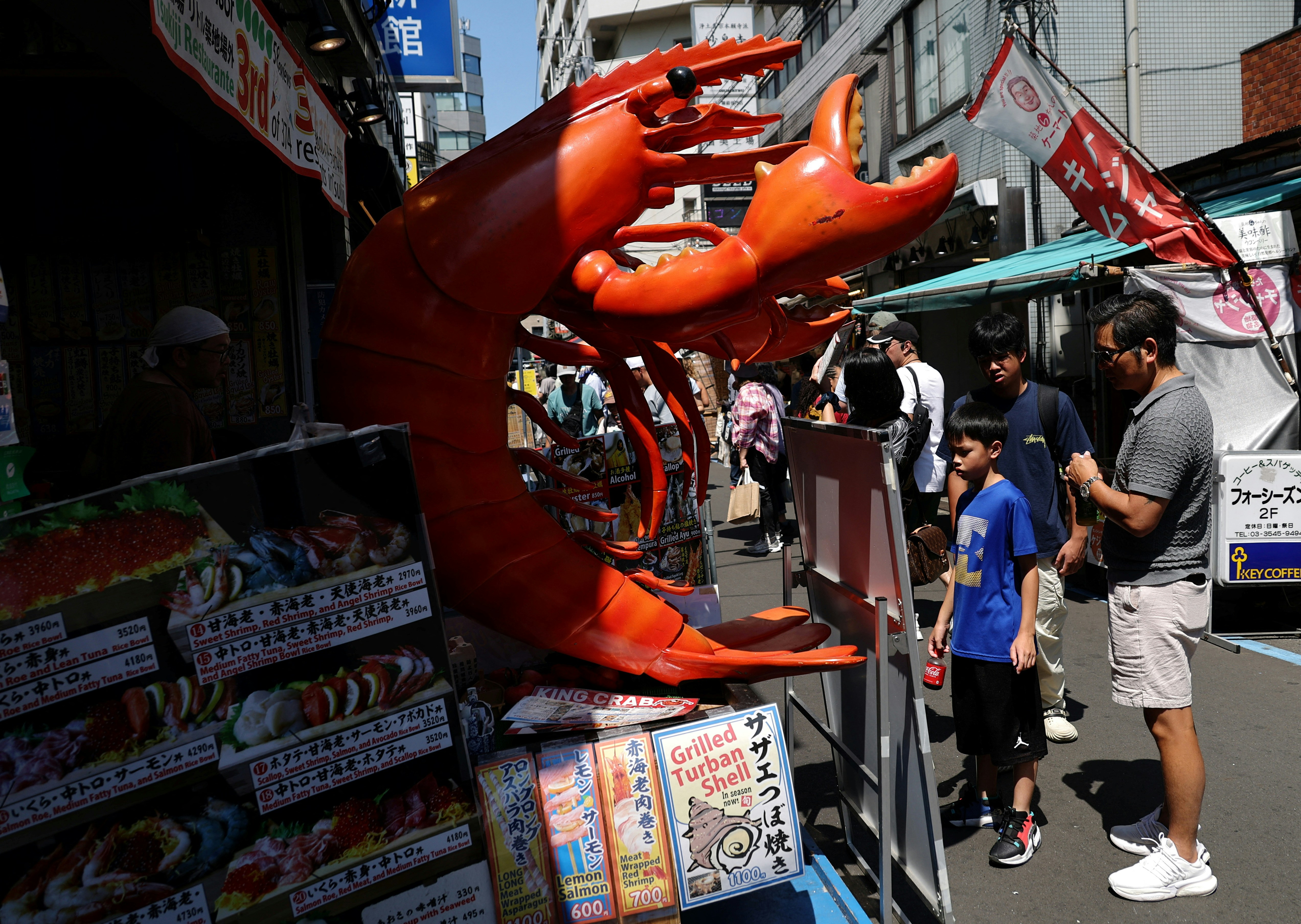 日本旅游・日本旅行・日本自由行・日本经济・日本旅游业・日本消费・东京・筑地：图为2024年6月14日，游客在日本东京筑地场外市场观看一家海鲜餐厅的招牌。（Reuters）