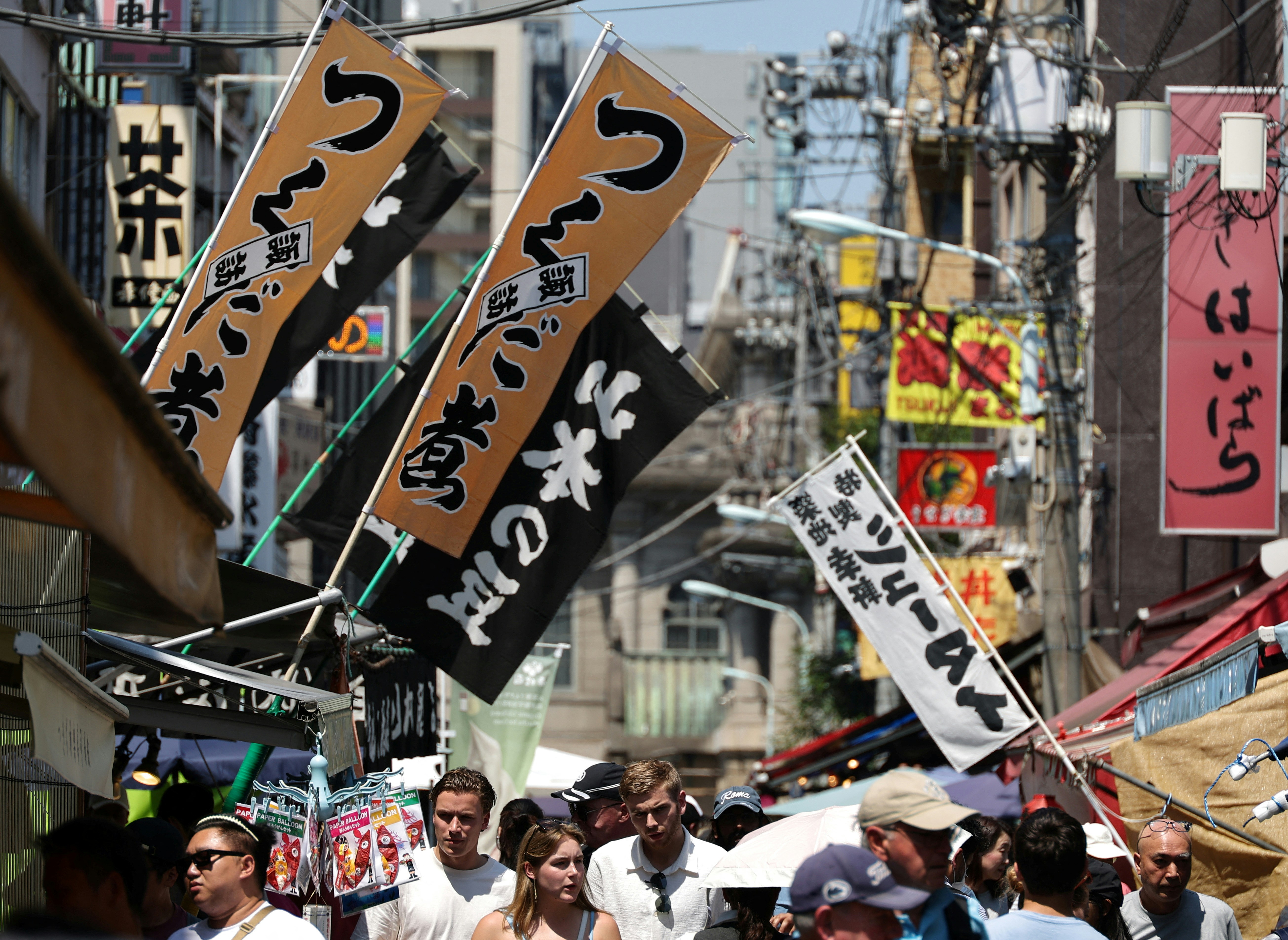 图为2024年6月14日，游客在日本东京筑地场外市场观看一家海鲜餐厅的招牌。（Reuters）