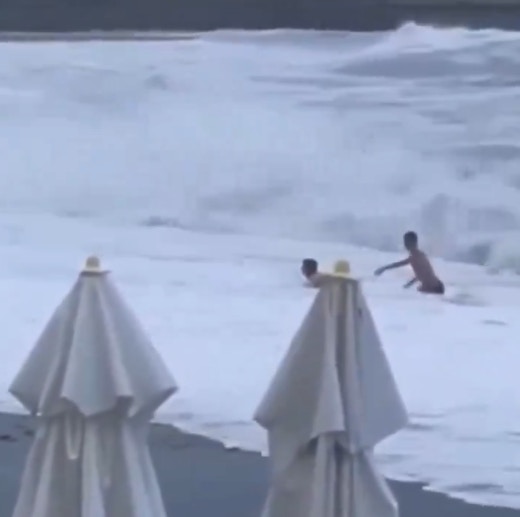 2人在水中挣扎，一度牵手想返回岸上，却再被海浪冲跌，女子来不及站起来之际，已被另一阵巨浪卷走。（影片截图）