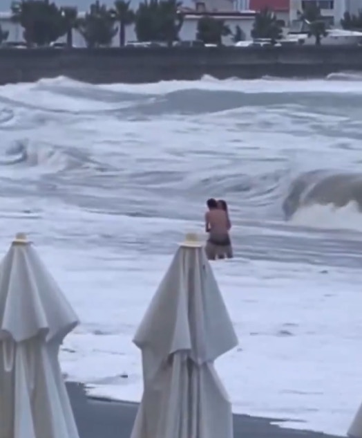 俄罗斯情侣日前到海边拍拖，2人停在近岸处热吻，却不知有巨浪正要袭来。（影片截图）