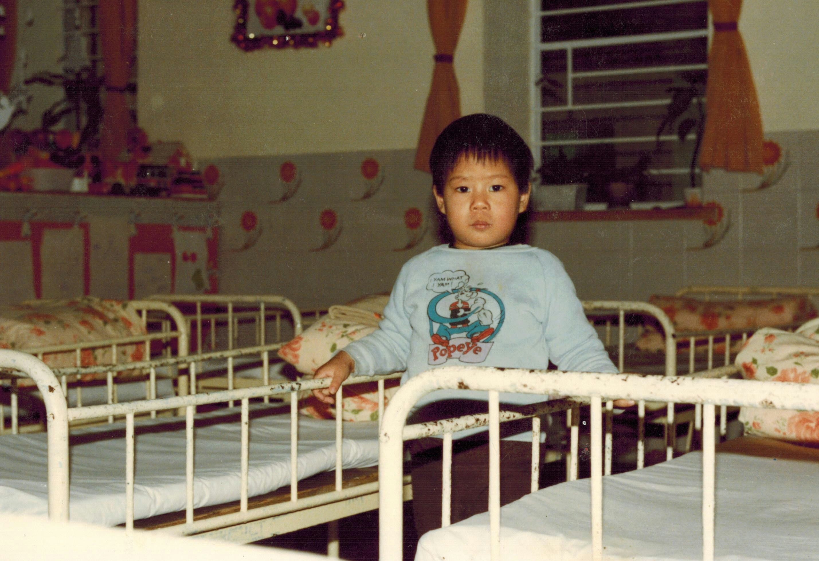年幼的陈伟杰站在家舍的铁架床堆中拍照。（受访者提供）