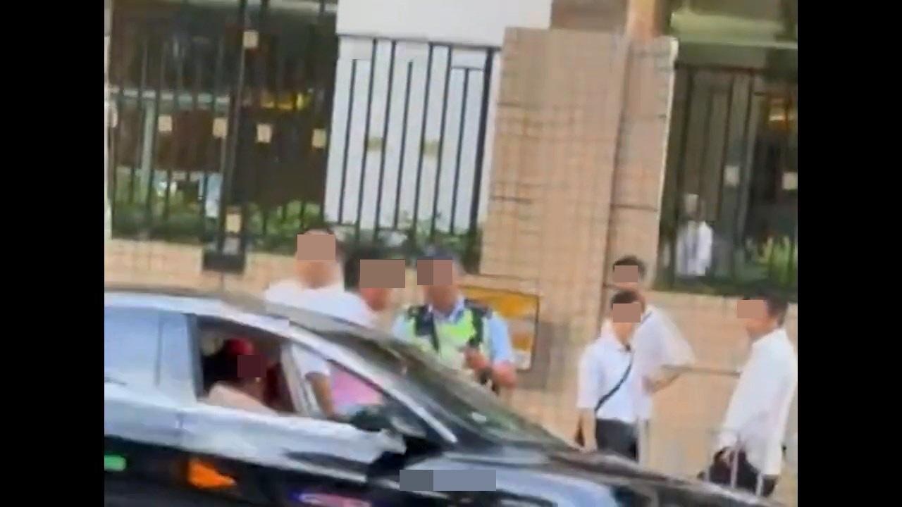 交通警员站在TESLA旁边，被多名白衣男子包围，车上司机更自称是「退休警司」，讥讽「有粒花先同我讲嘢啦，X样！」。（影片截图）